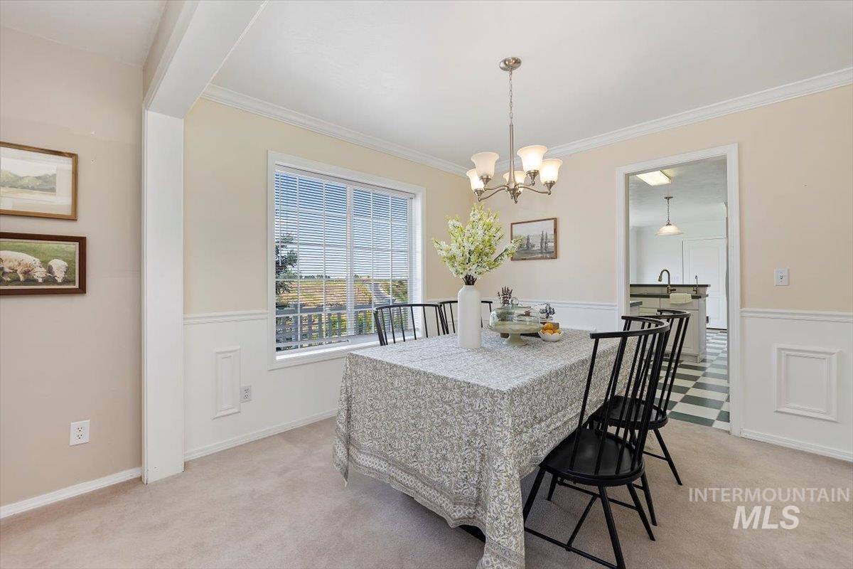 Dining space with light colored carpet, crown molding, a chandelier, and a wainscoted wall