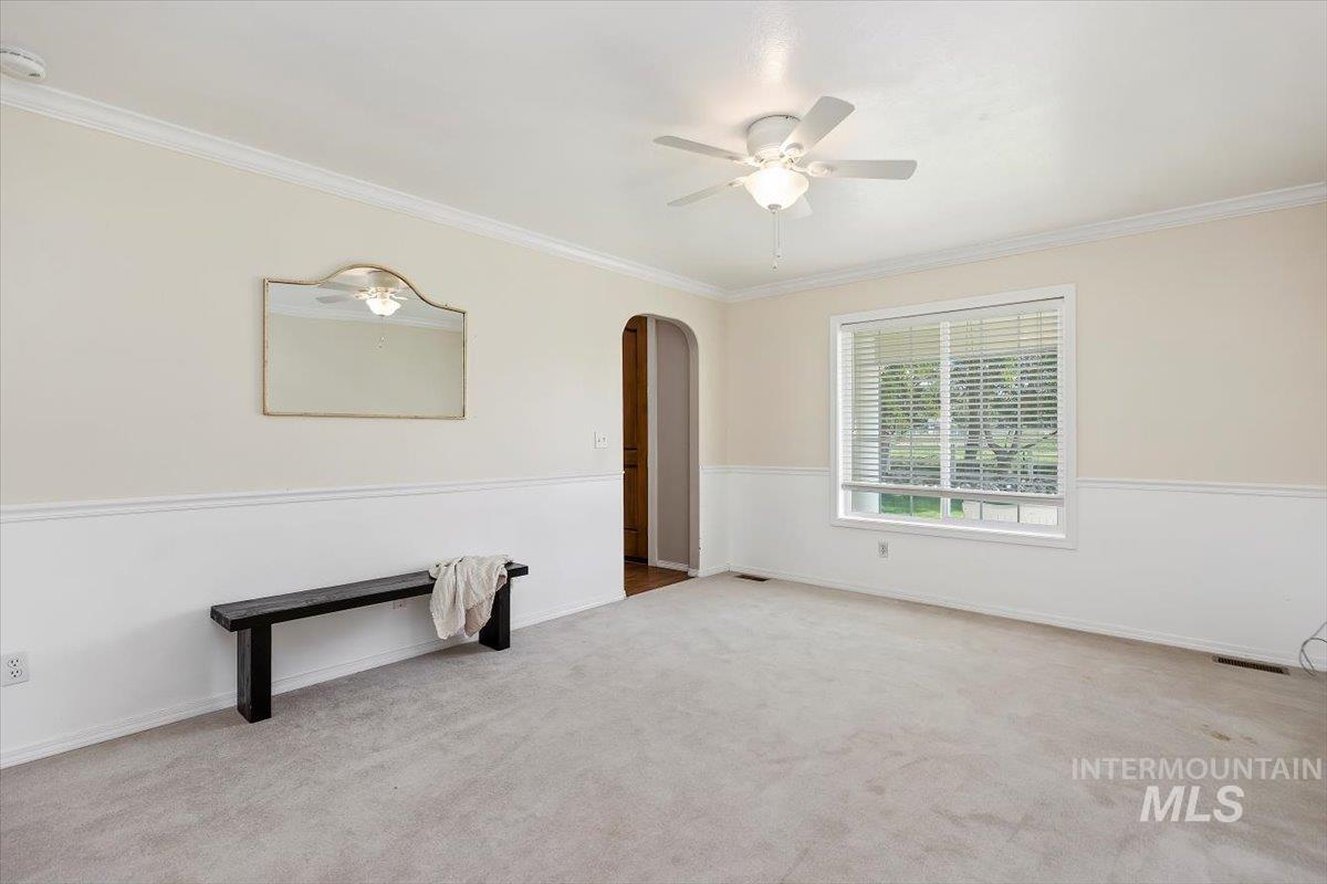 Carpeted spare room featuring ornamental molding, a ceiling fan, and arched walkways