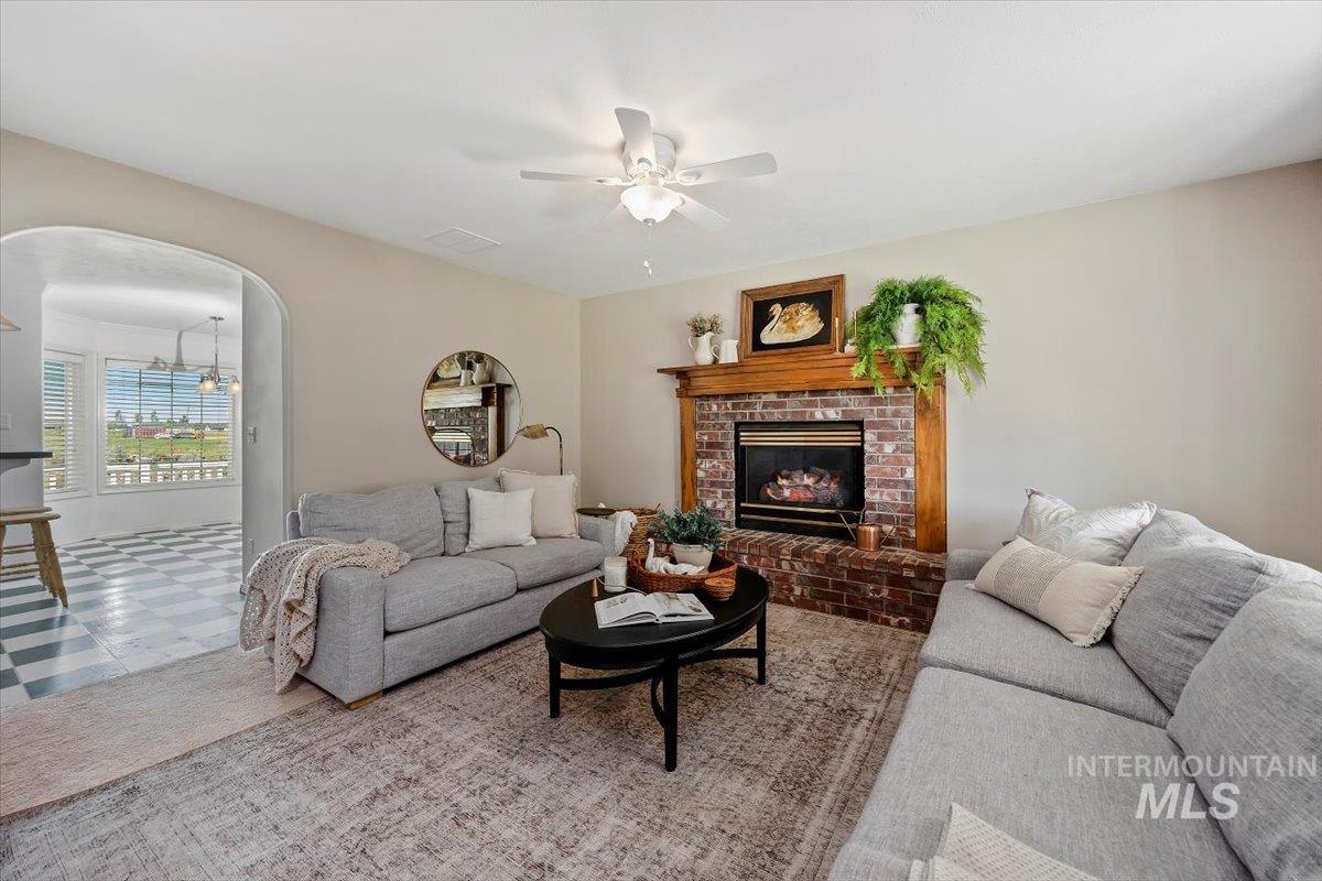 Living area with arched walkways, a ceiling fan, a brick fireplace, tile patterned floors, and a chandelier