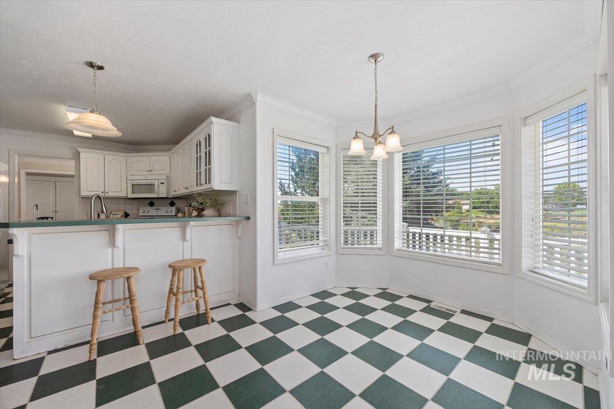 Kitchen with a breakfast bar area, glass insert cabinets, ornamental molding, light floors, and white cabinetry