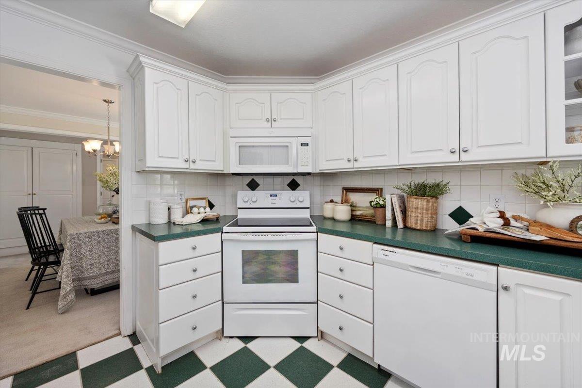 Kitchen with white appliances, dark countertops, white cabinets, tasteful backsplash, and crown molding