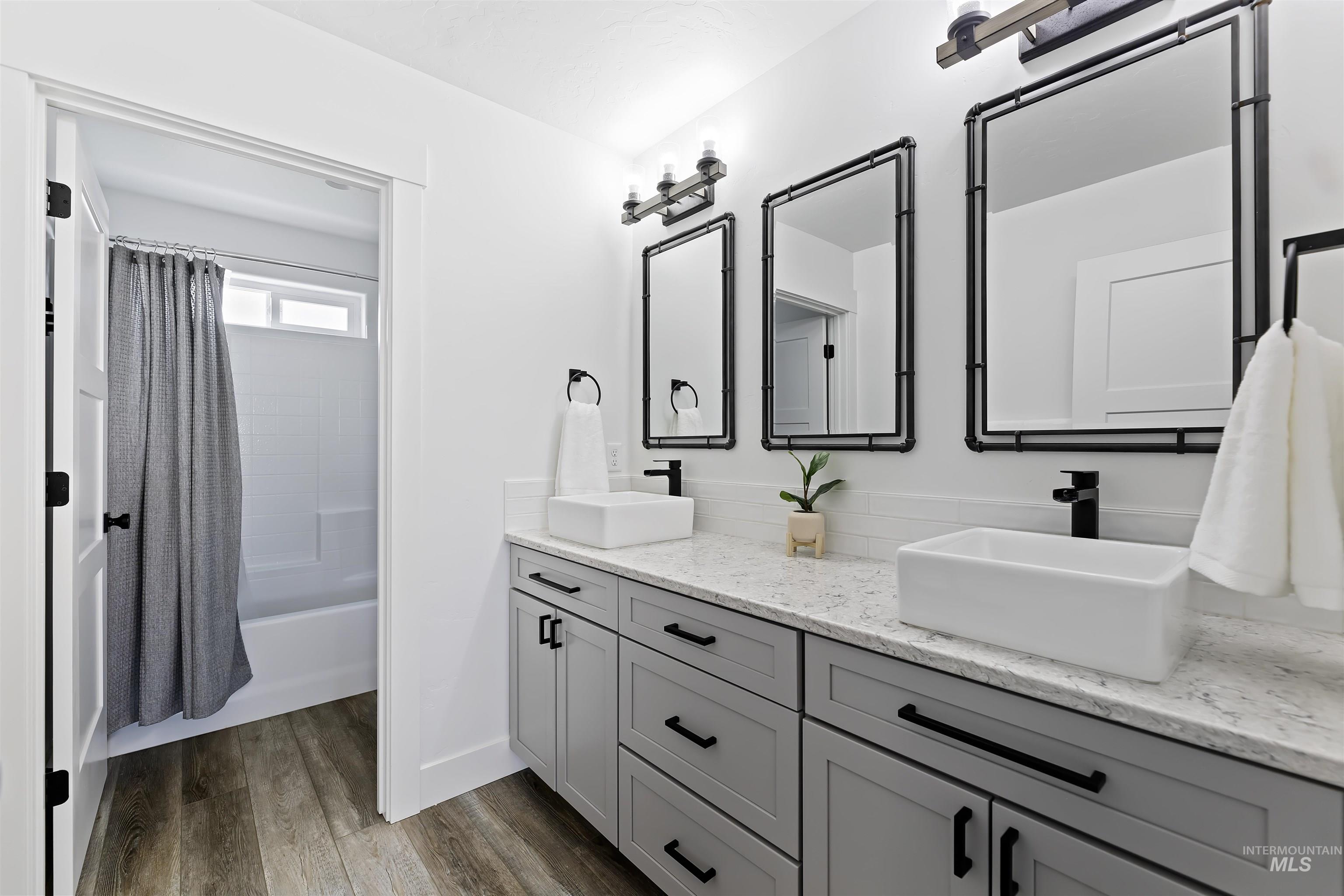 Full bathroom featuring shower / bathtub combination with curtain, double vanity, and dark wood-style flooring