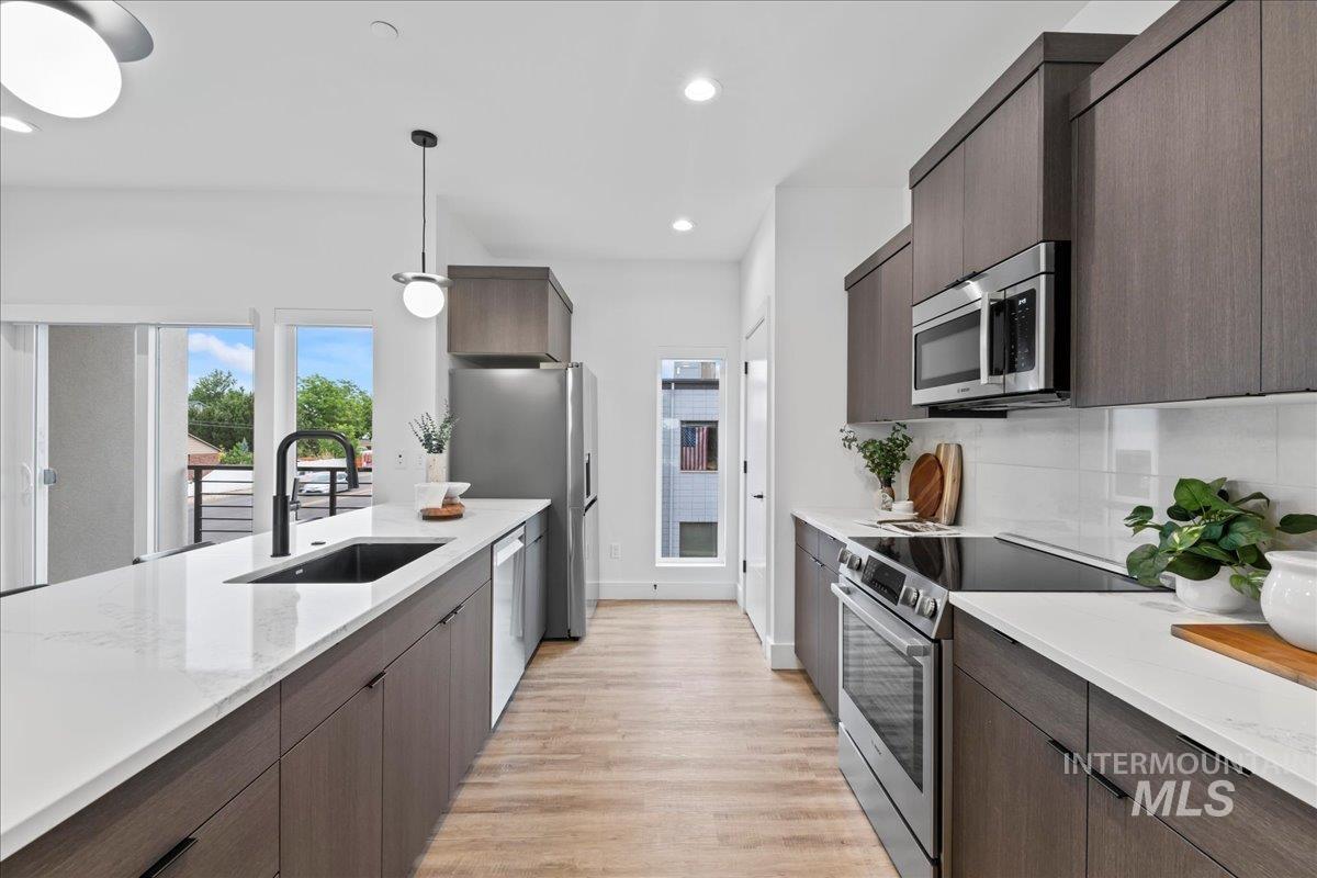 Kitchen featuring dark brown cabinets, modern cabinets, stainless steel appliances, light stone counters, and recessed lighting