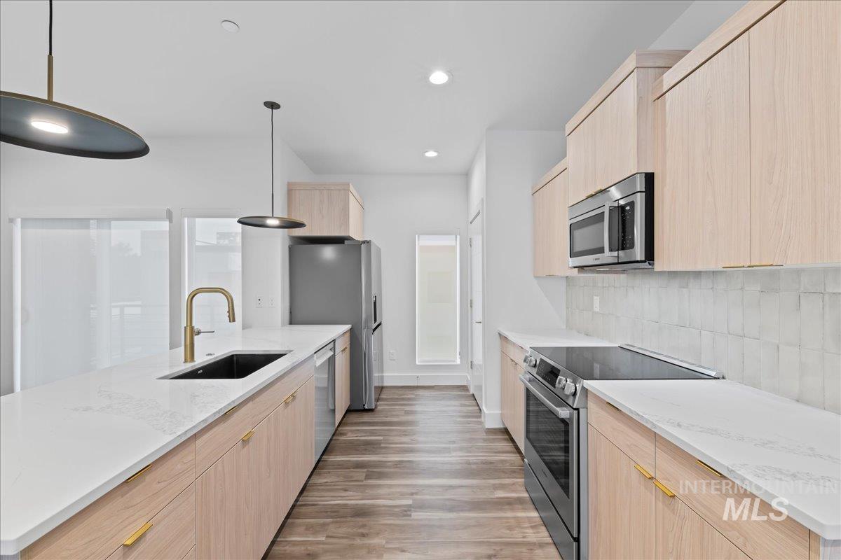 Kitchen with light brown cabinetry, light stone countertops, appliances with stainless steel finishes, modern cabinets, and recessed lighting