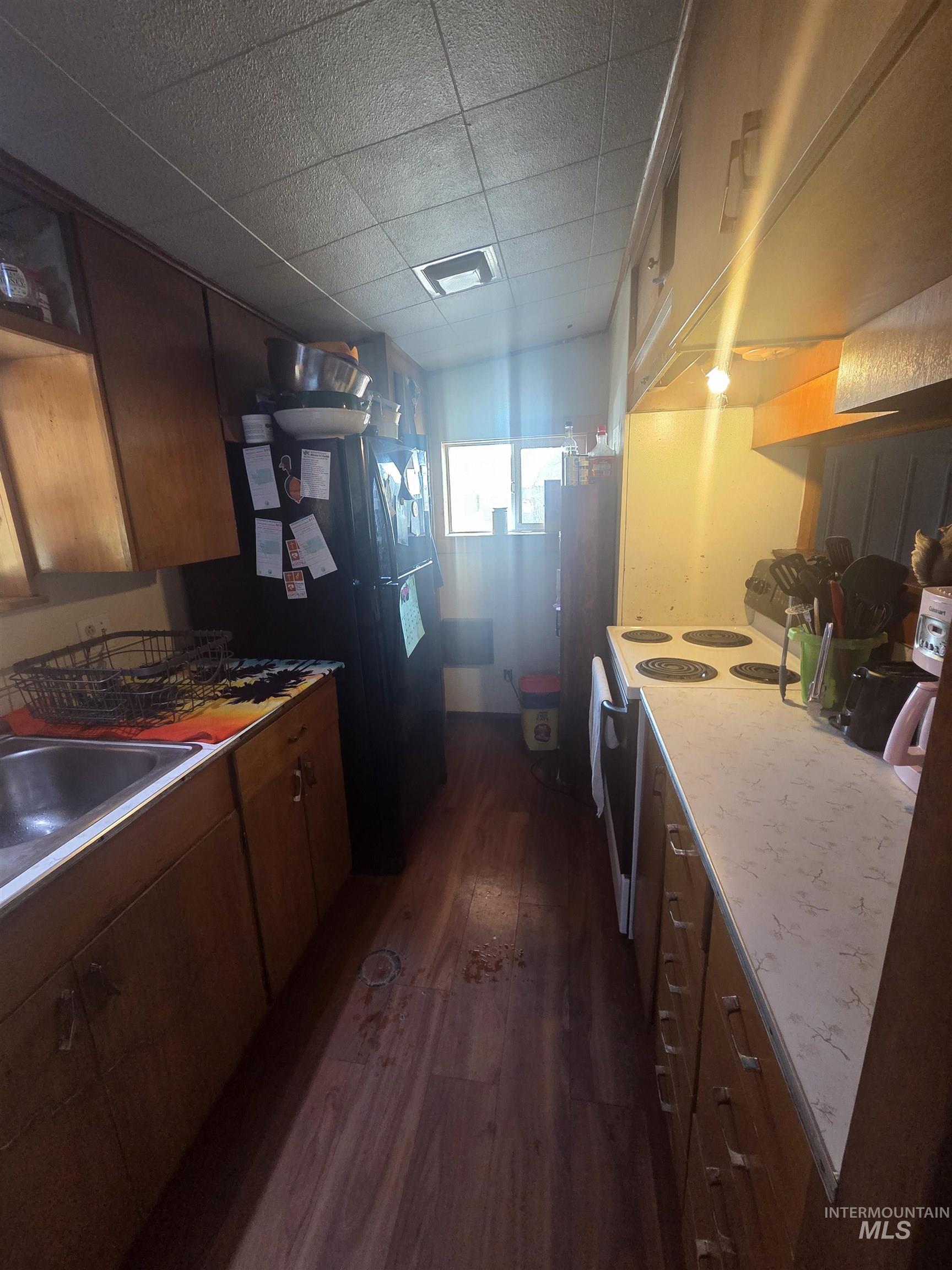 Kitchen with dark wood-style floors, white range with electric cooktop, freestanding refrigerator, brown cabinets, and fridge