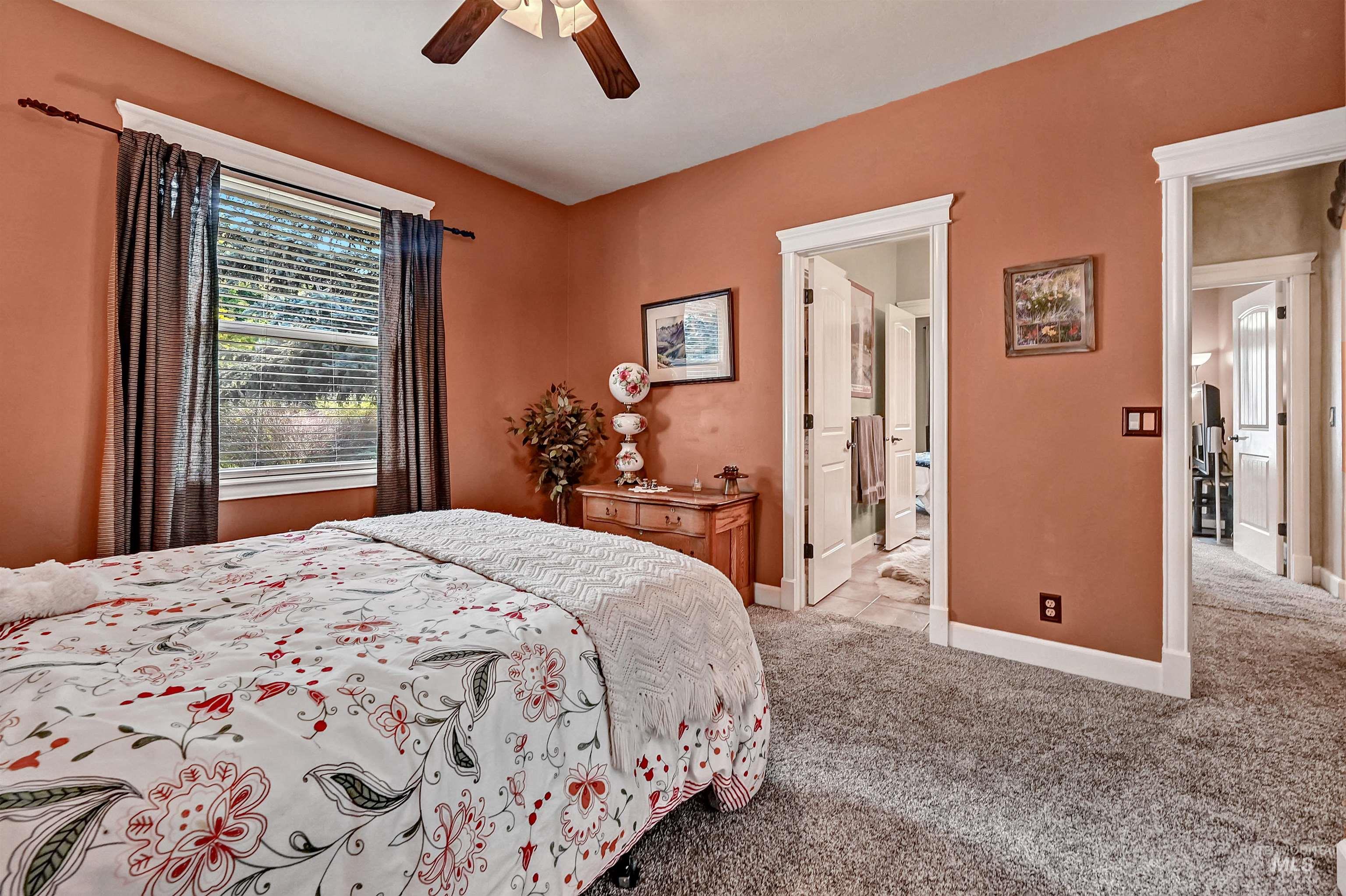 Bedroom with light colored carpet, ceiling fan, and connected bathroom