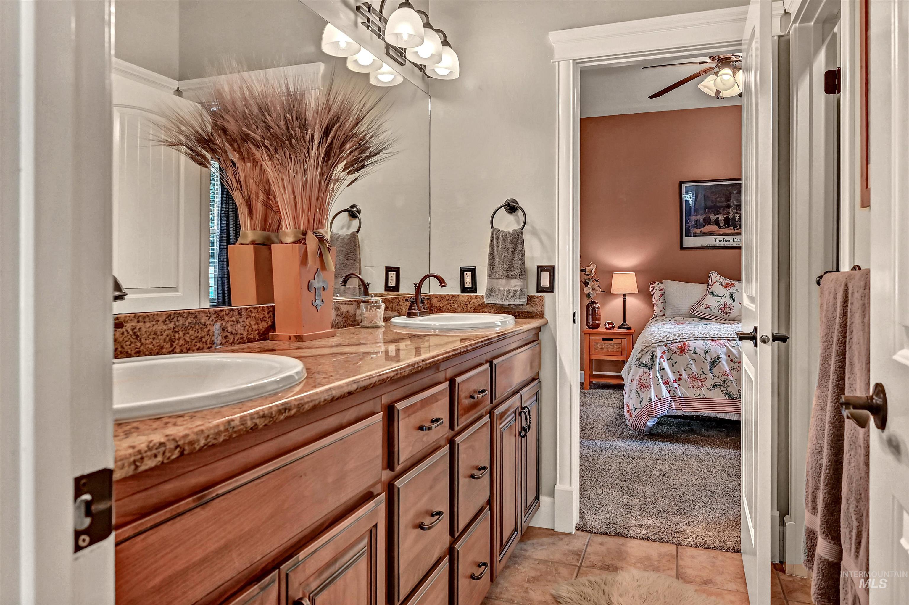 Ensuite bathroom with double vanity, light tile patterned flooring, ceiling fan, and a chandelier