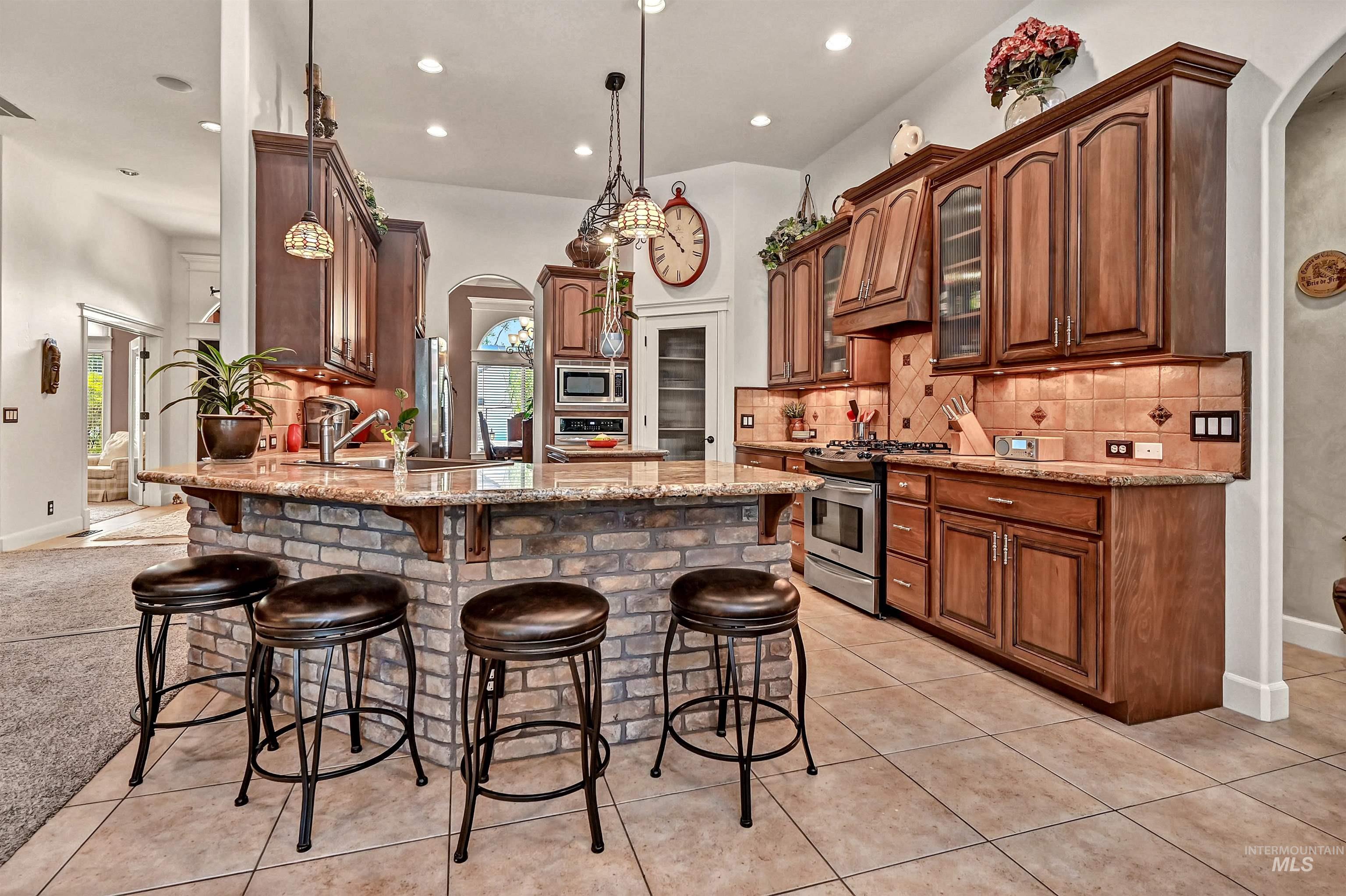 Kitchen featuring arched walkways, light stone counters, backsplash, a peninsula, and hanging light fixtures