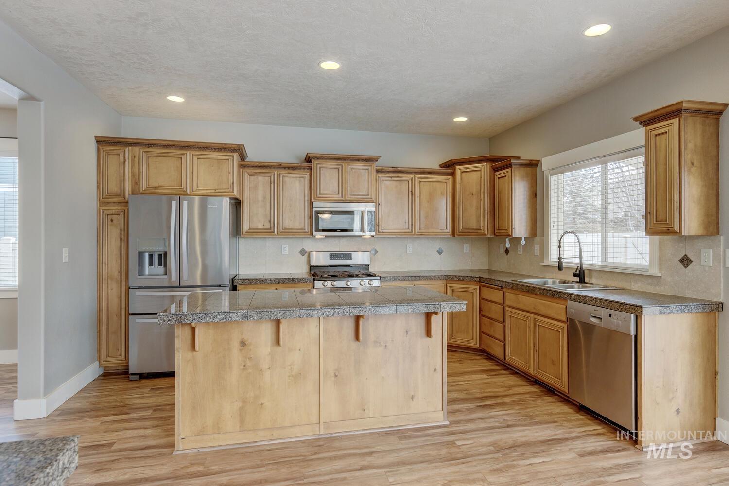 Kitchen featuring tile countertops, stainless steel appliances, tasteful backsplash, a breakfast bar area, and a center island