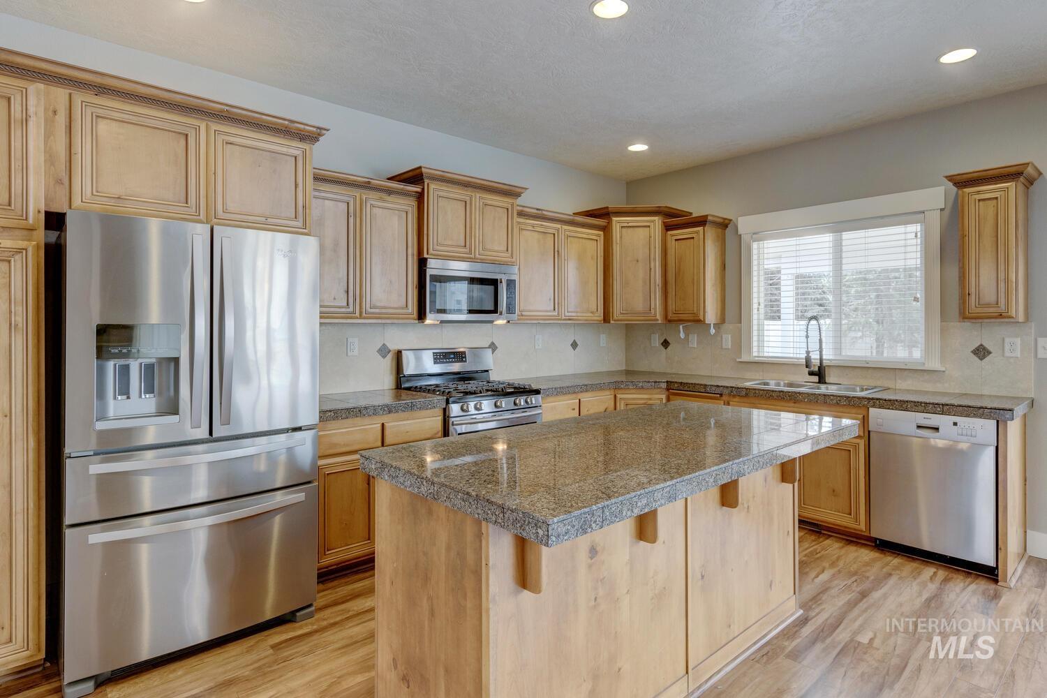 Kitchen with tile counters, appliances with stainless steel finishes, a center island, a kitchen breakfast bar, and light wood-type flooring