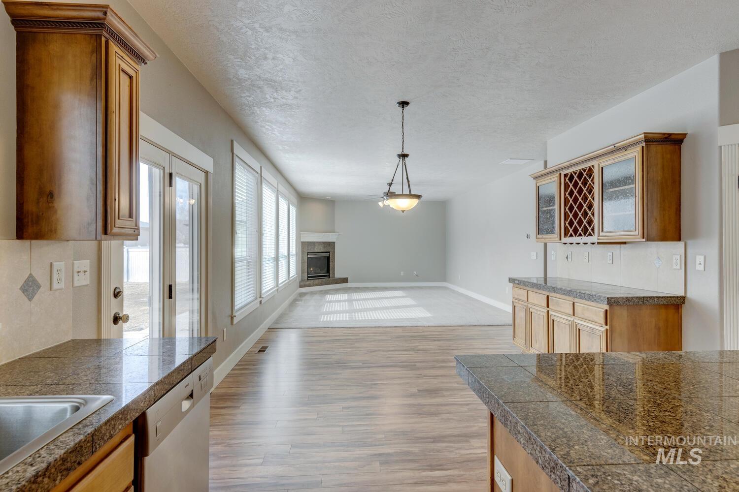 Kitchen with tile counters, pendant lighting, a textured ceiling, light wood finished floors, and white dishwasher