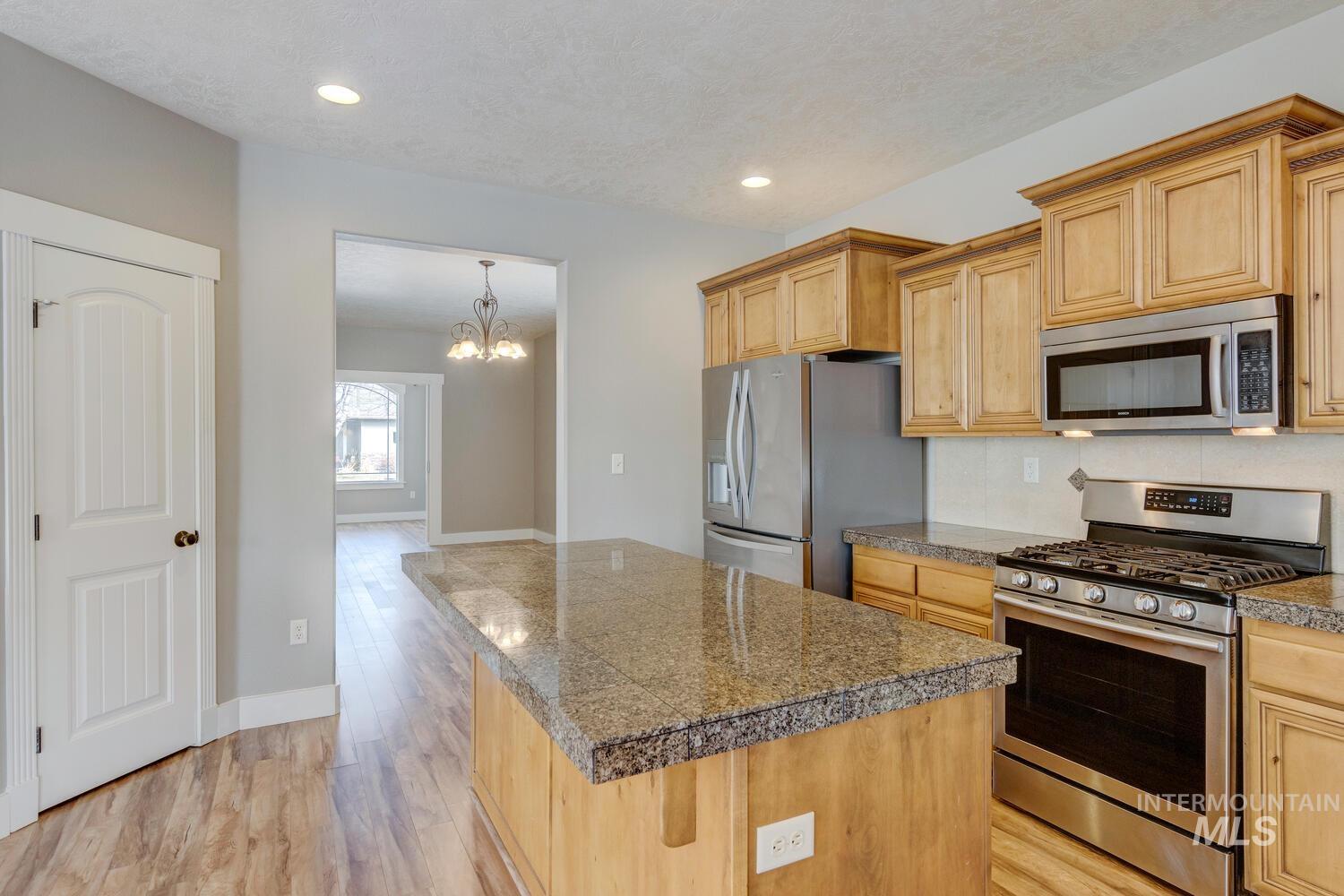 Kitchen featuring tile counters, stainless steel appliances, a kitchen island, light wood-style floors, and a chandelier