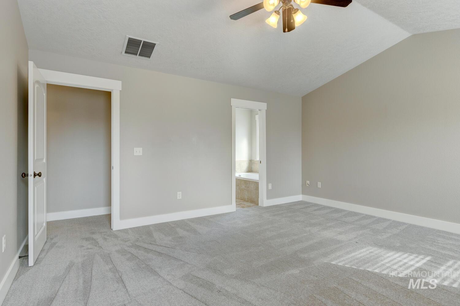 Unfurnished bedroom featuring light carpet, ensuite bath, a textured ceiling, ceiling fan, and vaulted ceiling