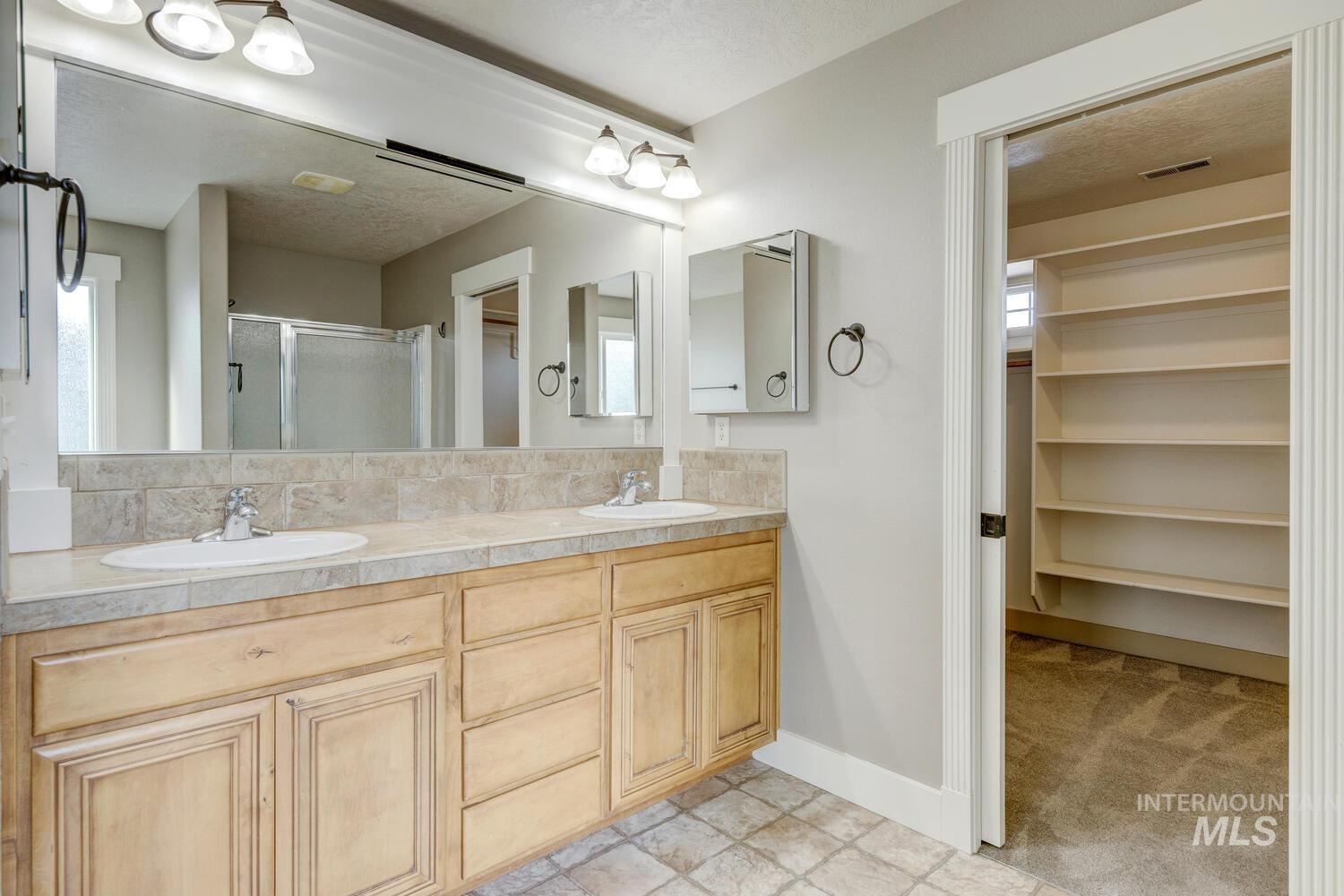 Full bath with a stall shower, a textured ceiling, double vanity, a closet, and healthy amount of natural light