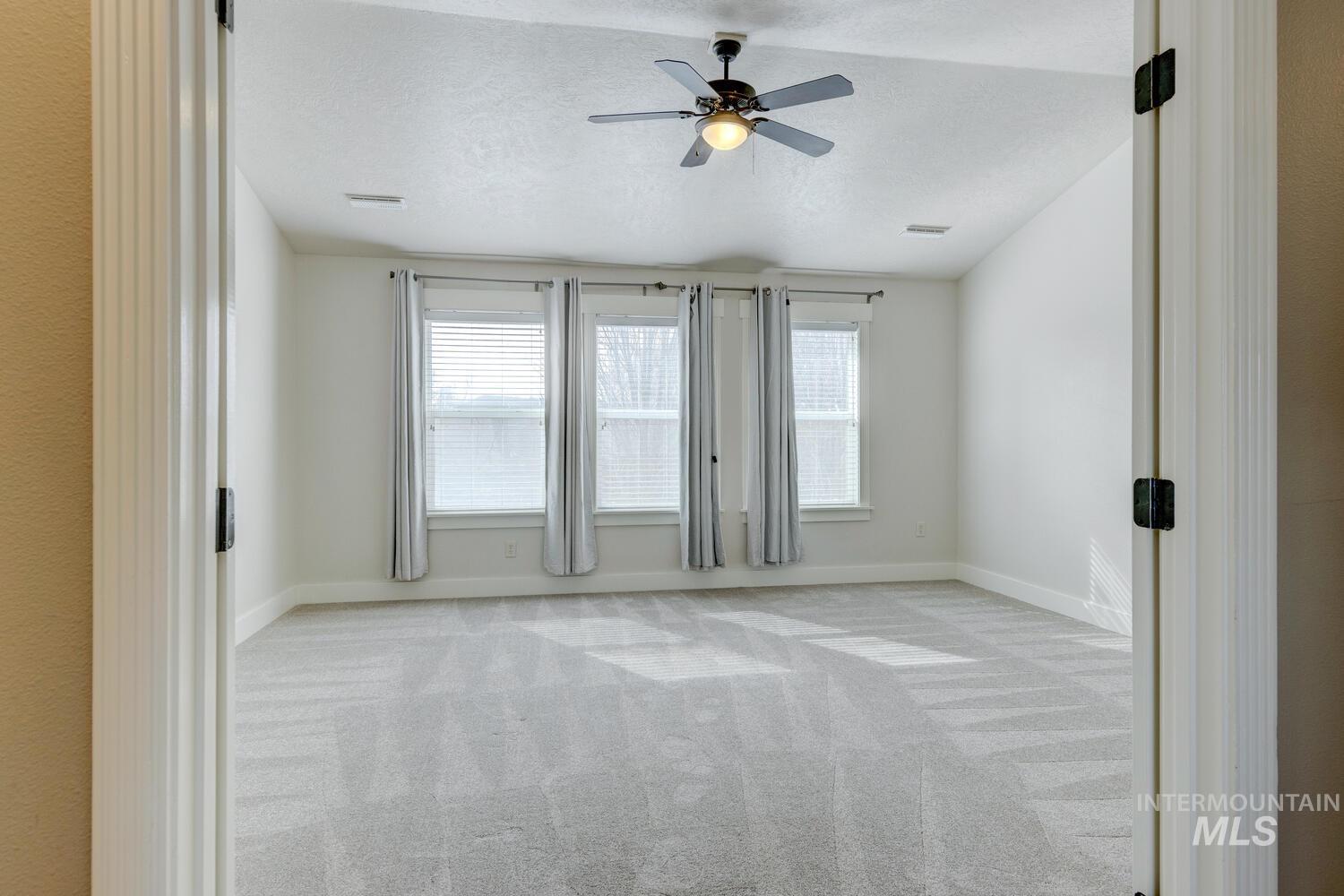 Unfurnished room with light colored carpet, plenty of natural light, a textured ceiling, and a ceiling fan