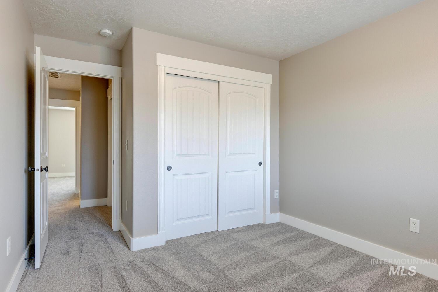 Unfurnished bedroom with light colored carpet, a textured ceiling, and a closet