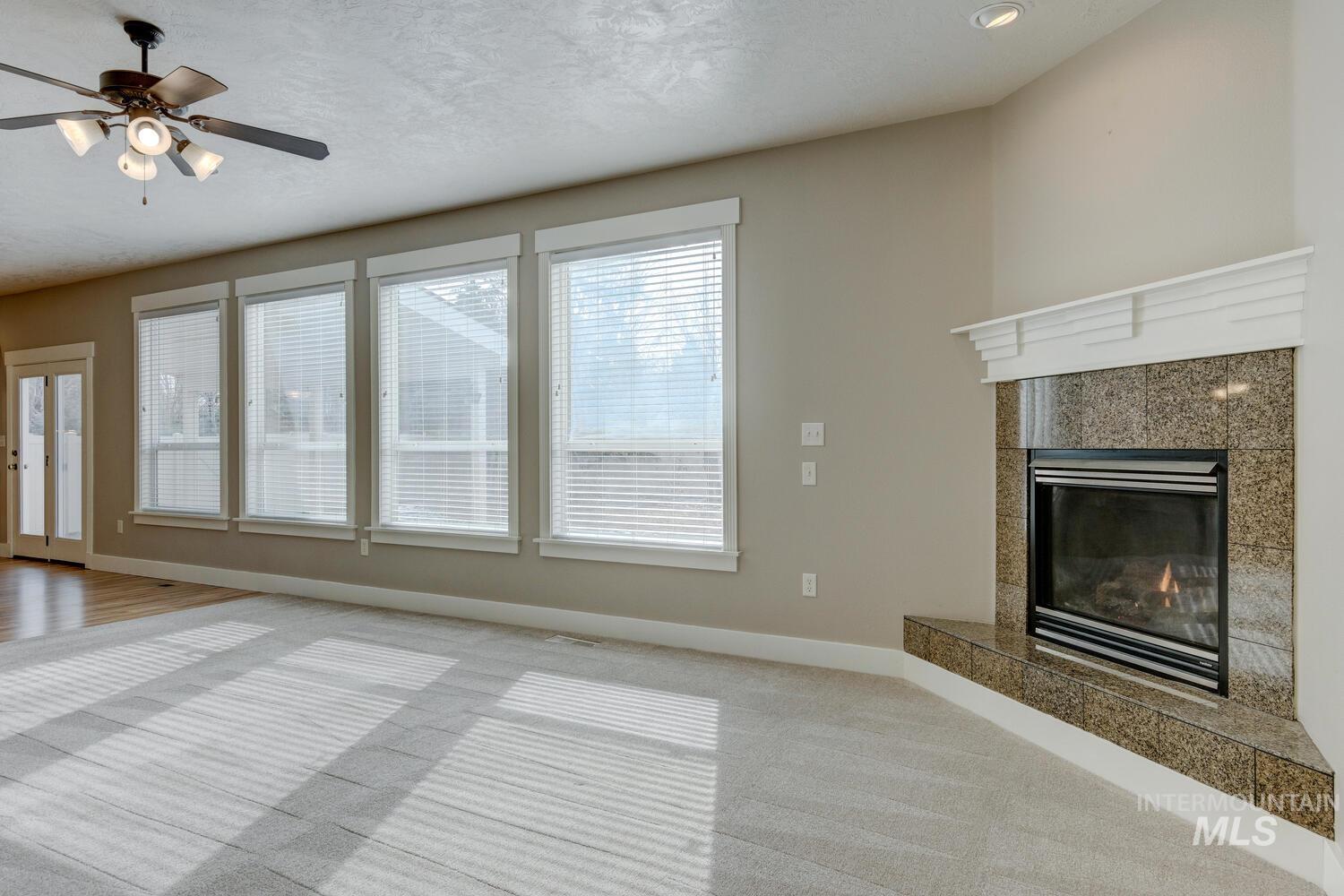Unfurnished living room with a high end fireplace, carpet floors, a ceiling fan, and a textured ceiling
