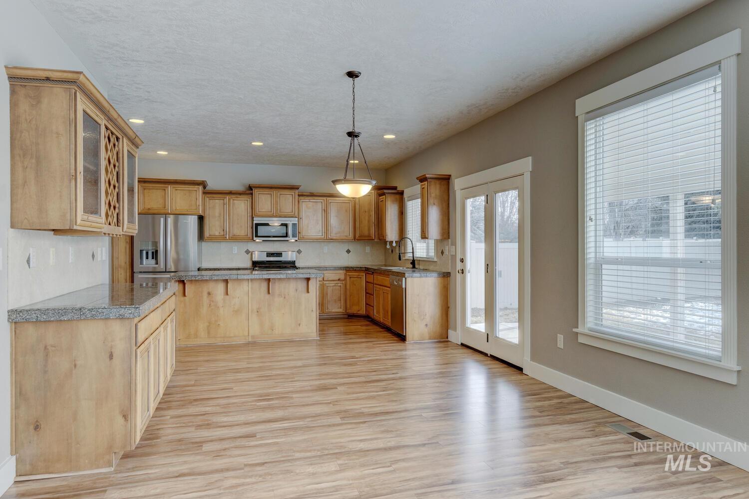Kitchen with glass insert cabinets, light wood-style floors, pendant lighting, a kitchen island, and recessed lighting
