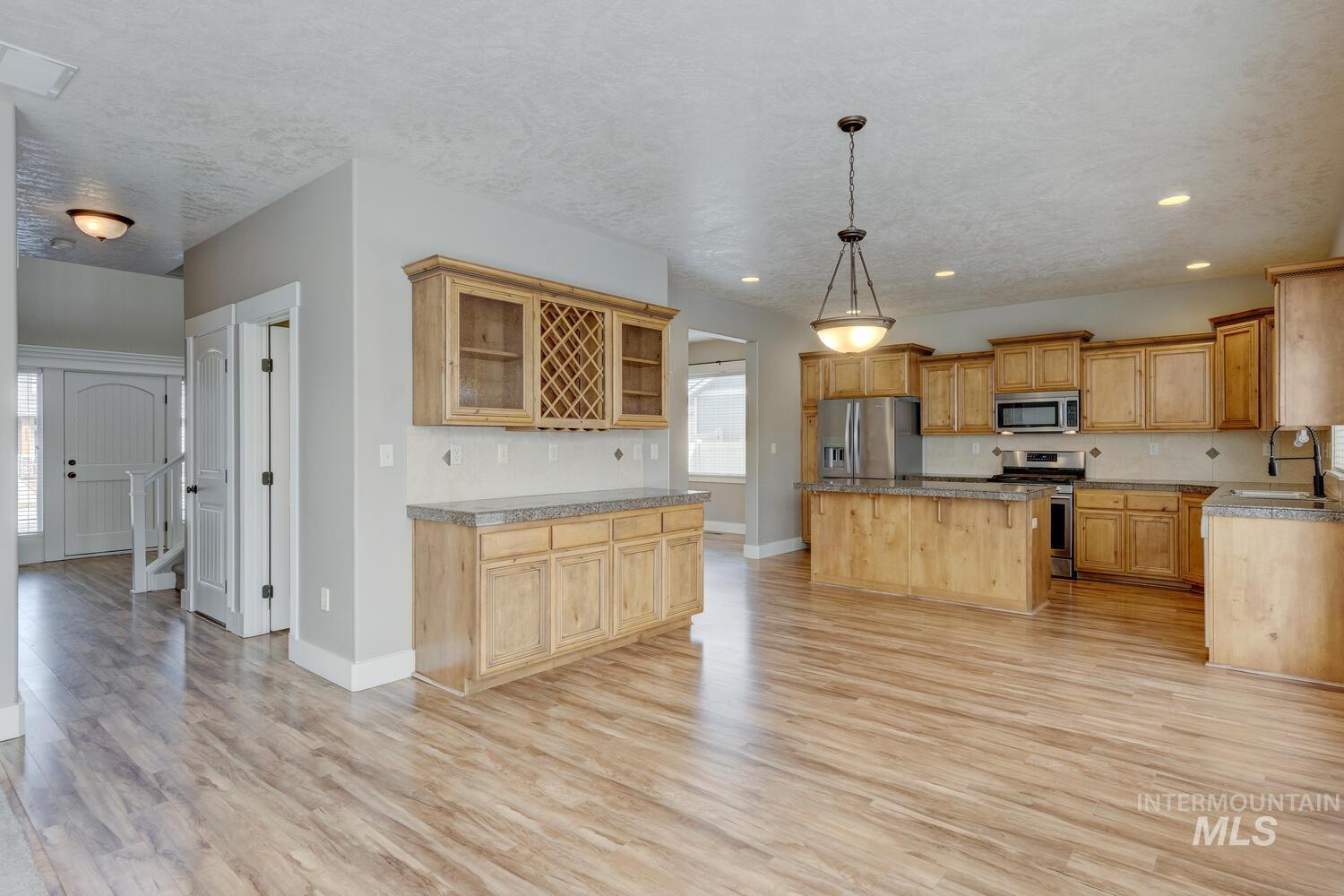 Kitchen featuring pendant lighting, backsplash, light wood-style flooring, a kitchen island, and appliances with stainless steel finishes