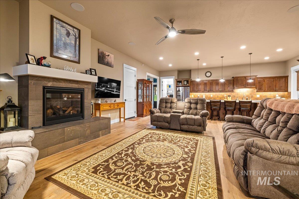 Living room featuring ceiling fan, light wood-type flooring, a tiled fireplace, and recessed lighting