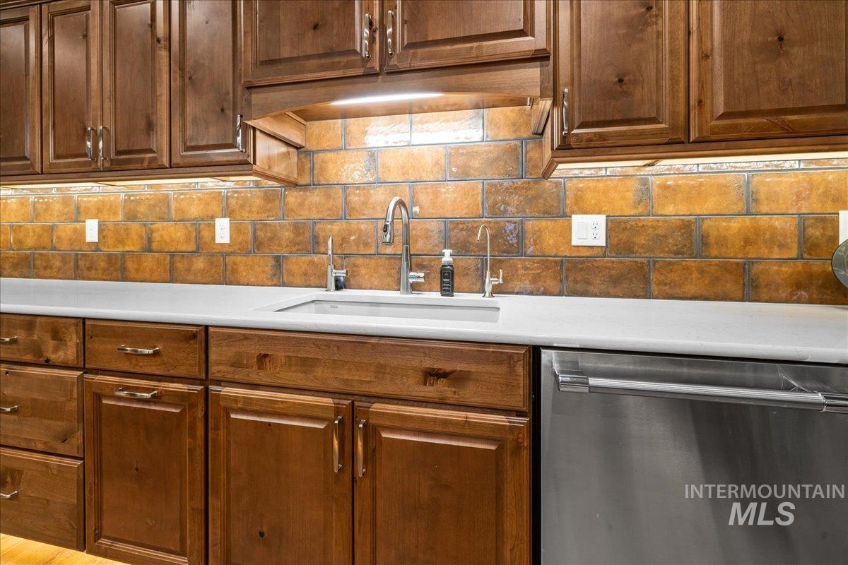 Kitchen featuring stainless steel dishwasher, tasteful backsplash, light countertops, and brown cabinetry