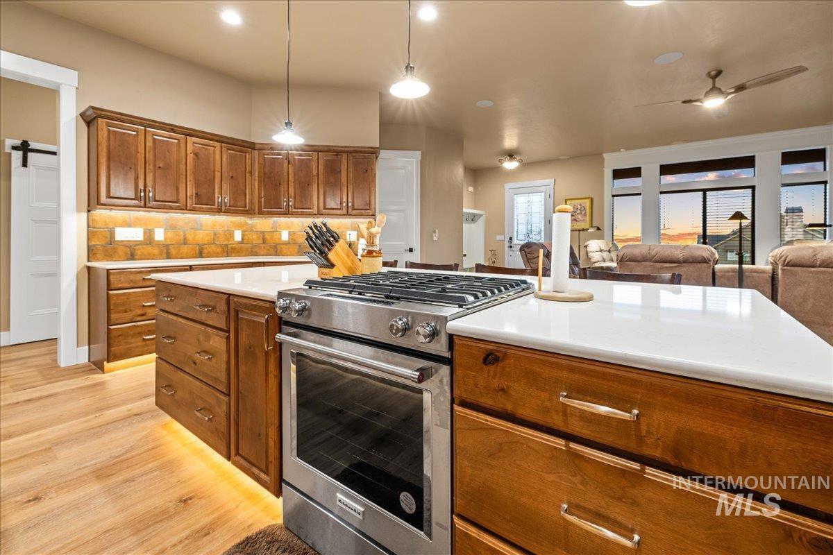 Kitchen with stainless steel gas range oven, brown cabinets, hanging light fixtures, tasteful backsplash, and a barn door