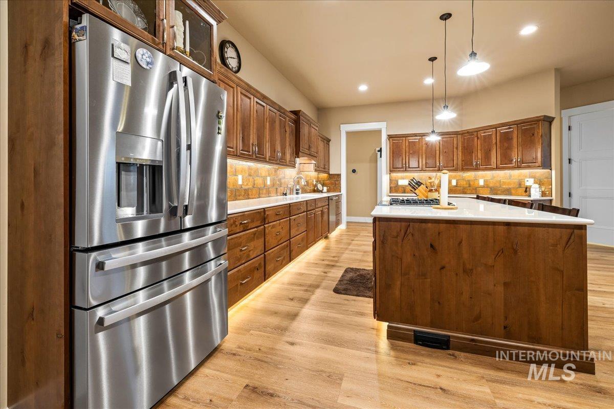 Kitchen featuring stainless steel fridge with ice dispenser, hanging light fixtures, a center island, light wood finished floors, and recessed lighting