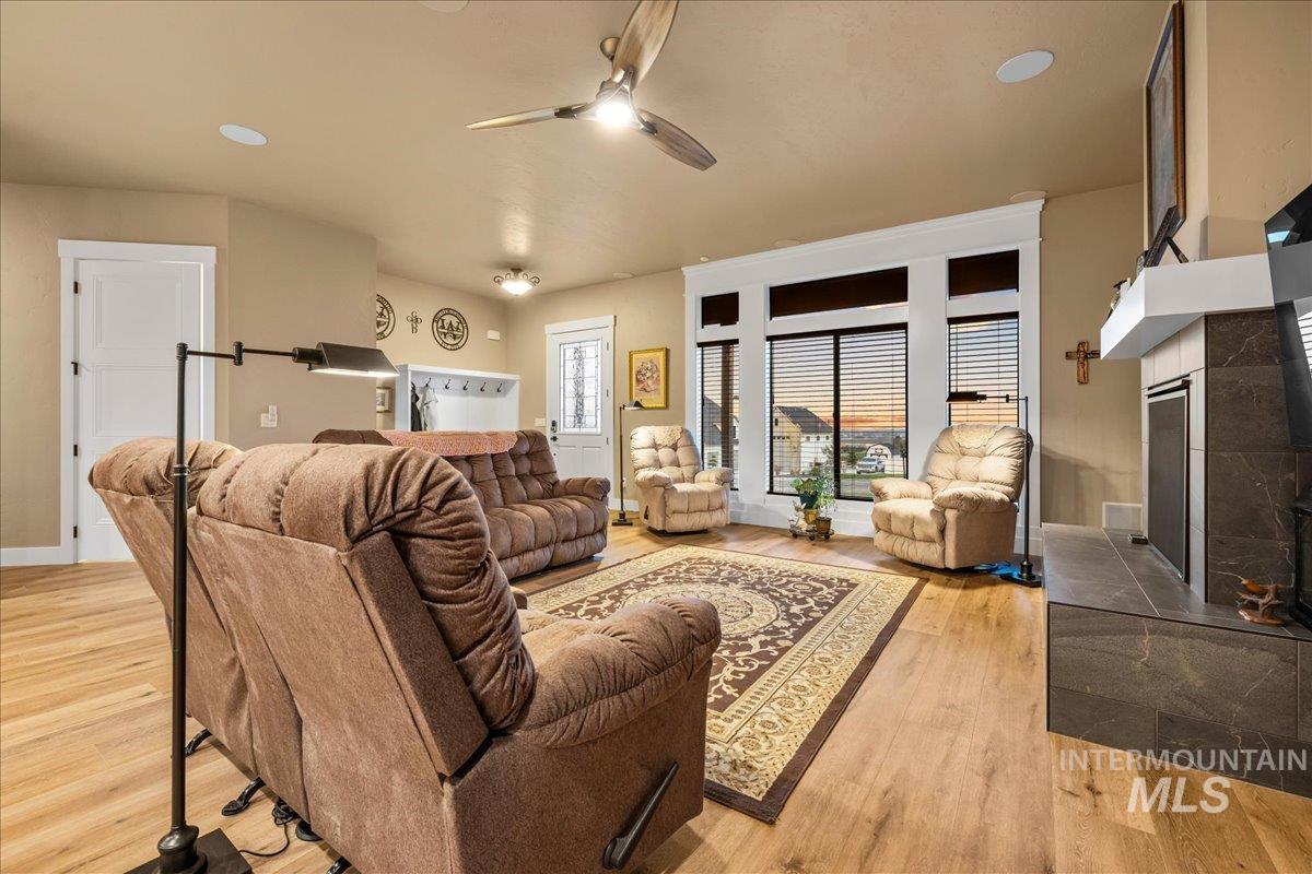 Living room featuring a tiled fireplace, light wood finished floors, a ceiling fan, and recessed lighting