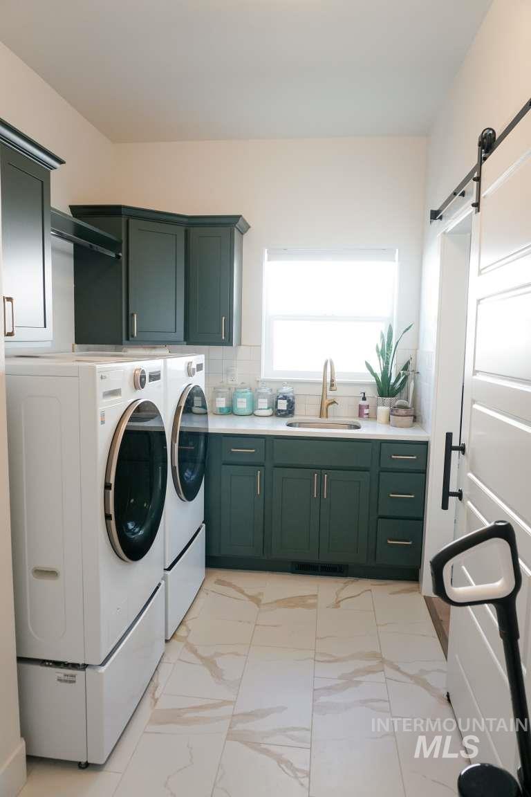 Washroom with a barn door, light marble finish floors, washing machine and dryer, and cabinet space