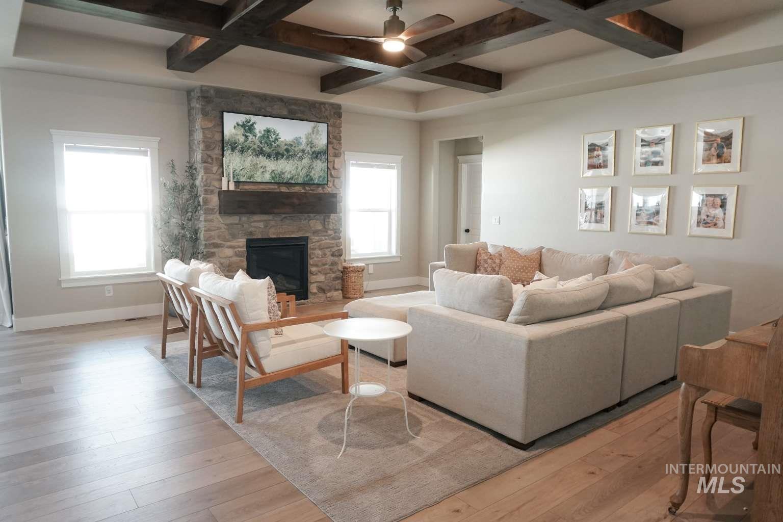 Living area featuring coffered ceiling, light wood-style floors, beam ceiling, ceiling fan, and a fireplace