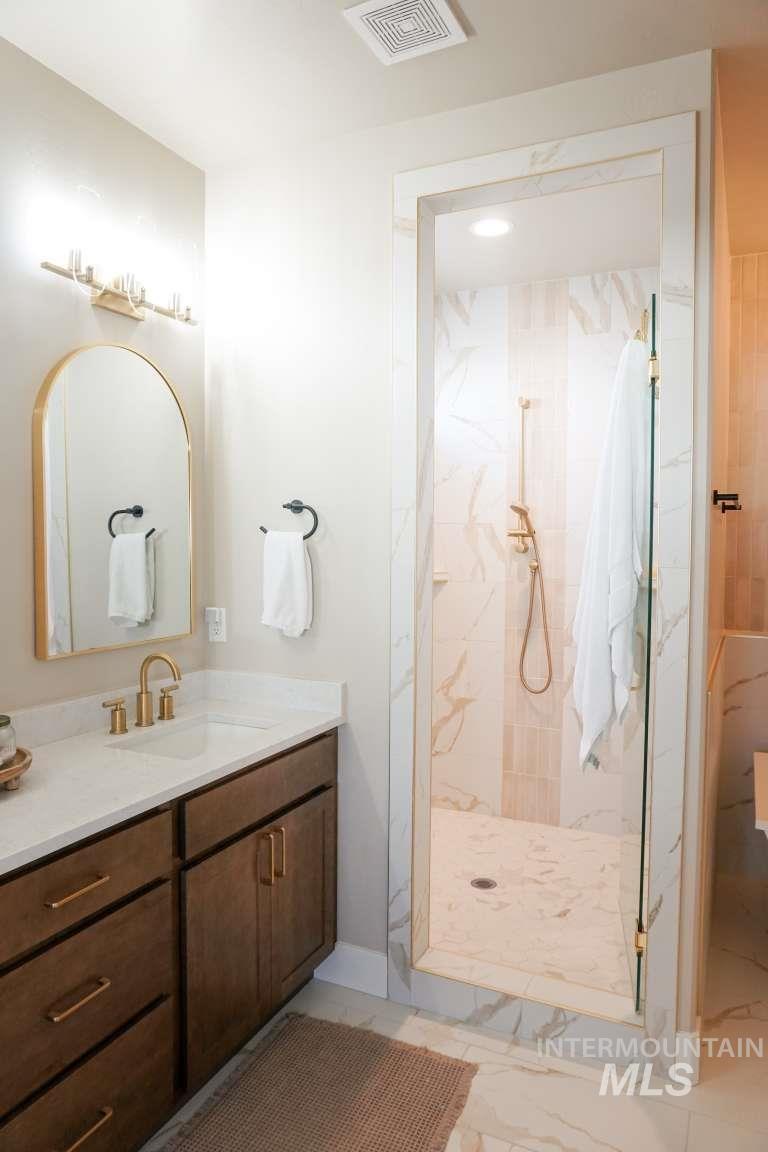 Full bath featuring vanity, a marble finish shower, and light marble finish floors