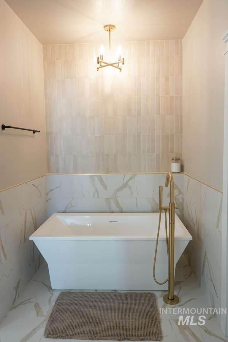 Bathroom with tile walls, marble look tiles, a freestanding tub, and a wainscoted wall