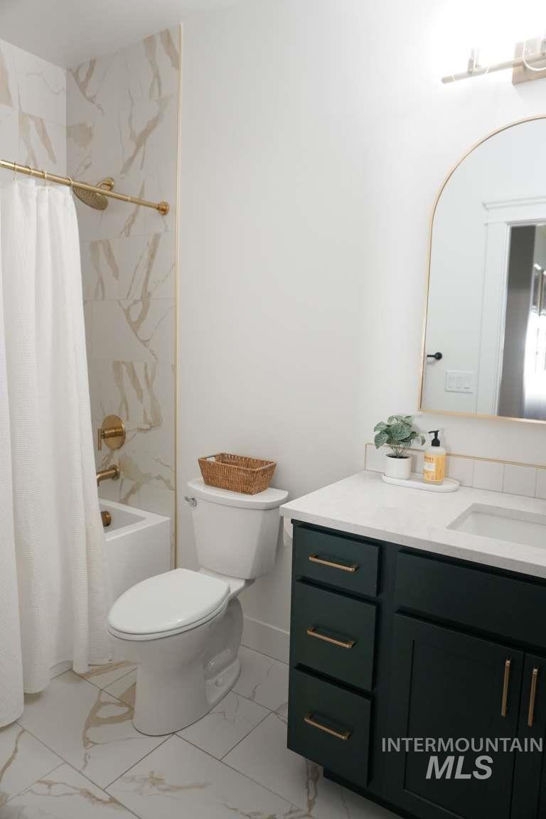 Bathroom featuring vanity, shower / tub combo, and light marble finish flooring