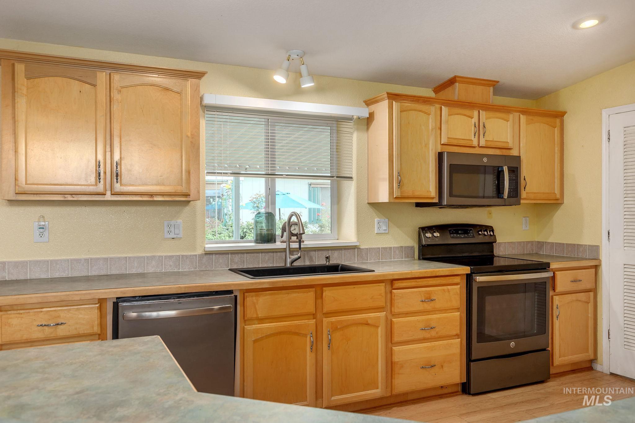 Kitchen with stainless steel appliances, light countertops, light brown cabinets, light wood-style floors, and recessed lighting