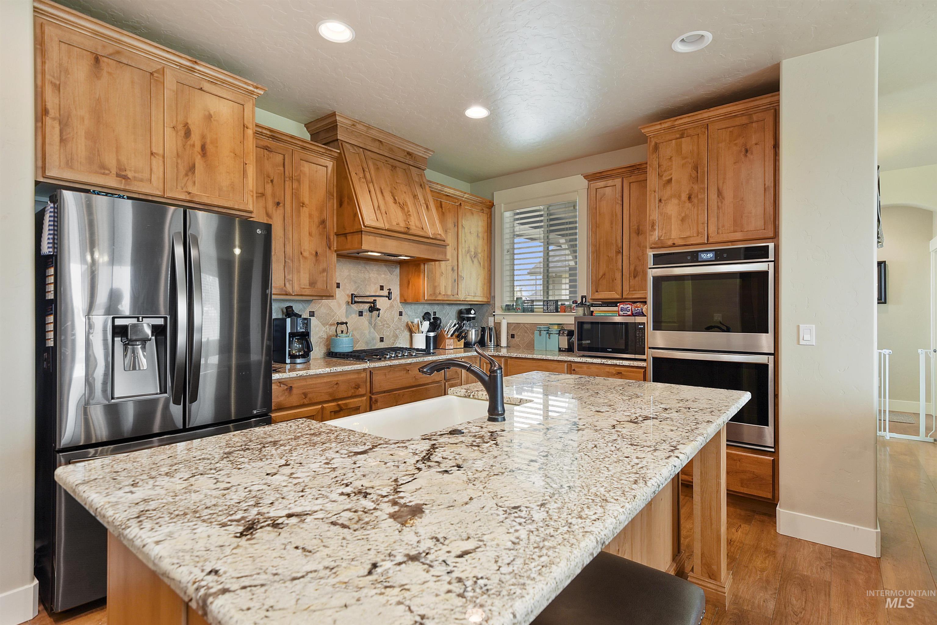 Kitchen with backsplash, appliances with stainless steel finishes, light stone countertops, light wood finished floors, and recessed lighting