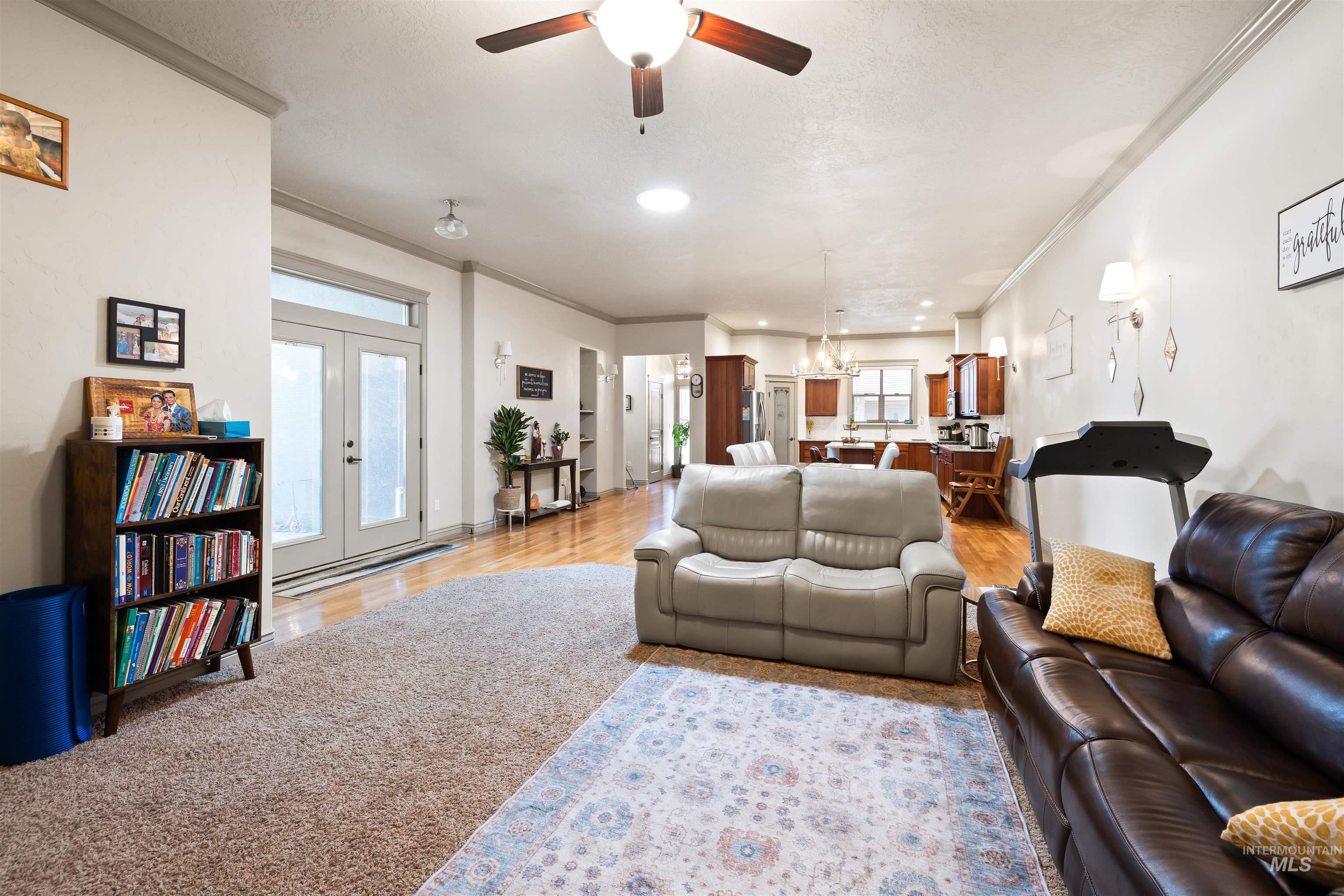 Living area with healthy amount of natural light, ornamental molding, french doors, ceiling fan, and light wood-style flooring