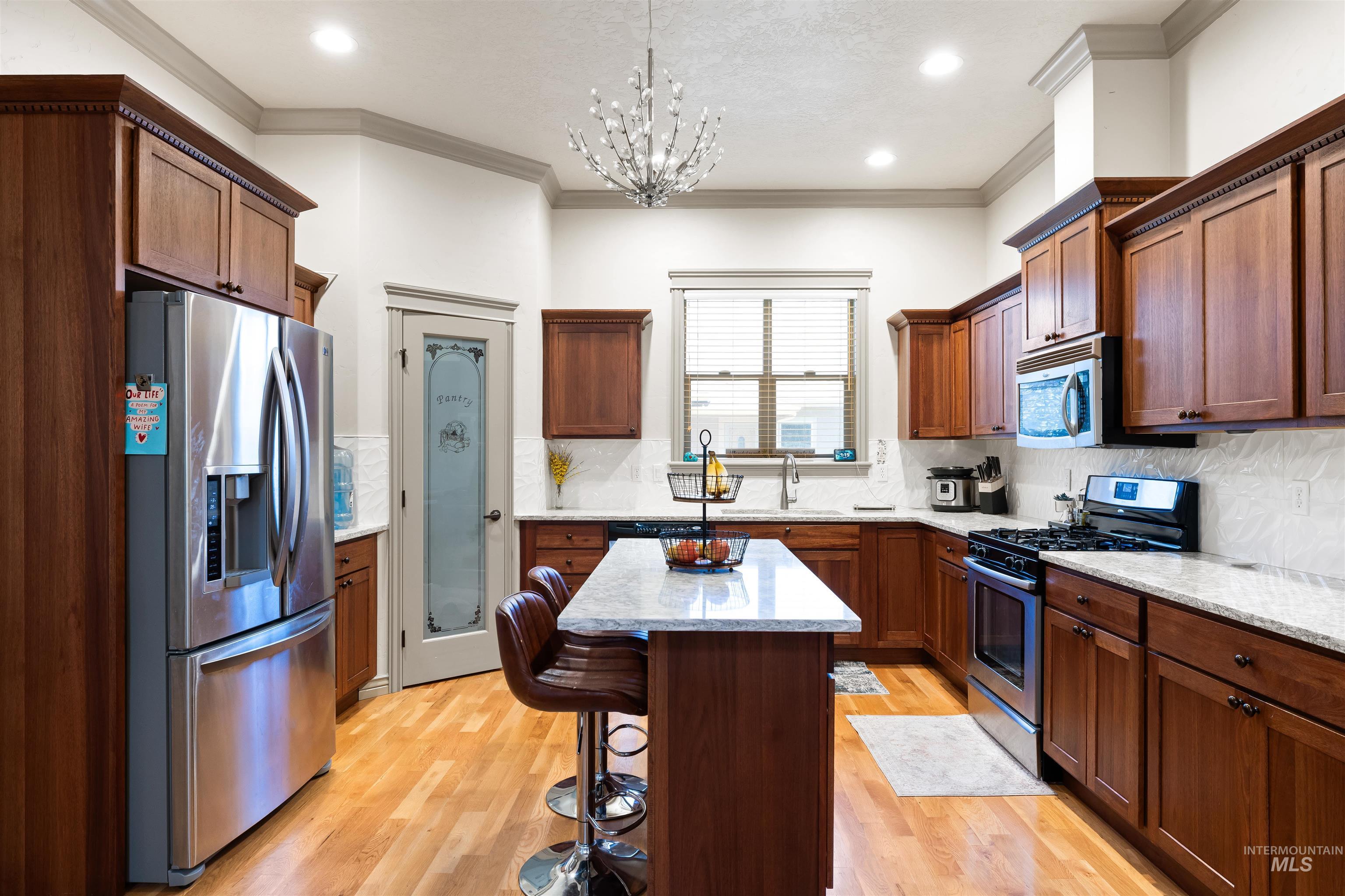 Kitchen with stainless steel appliances, backsplash, light wood finished floors, light stone countertops, and decorative light fixtures