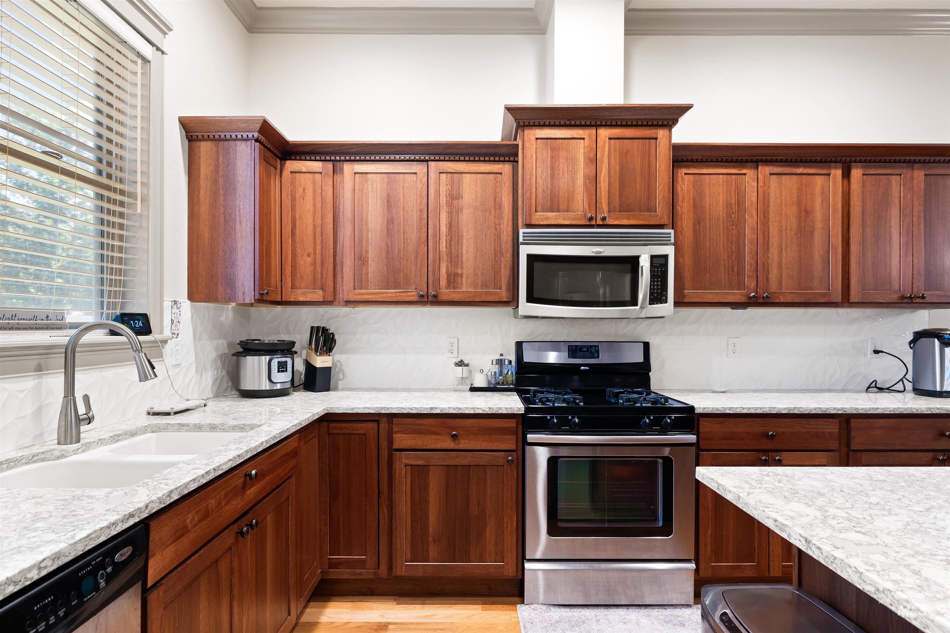 Kitchen featuring appliances with stainless steel finishes, brown cabinets, light stone countertops, crown molding, and decorative backsplash