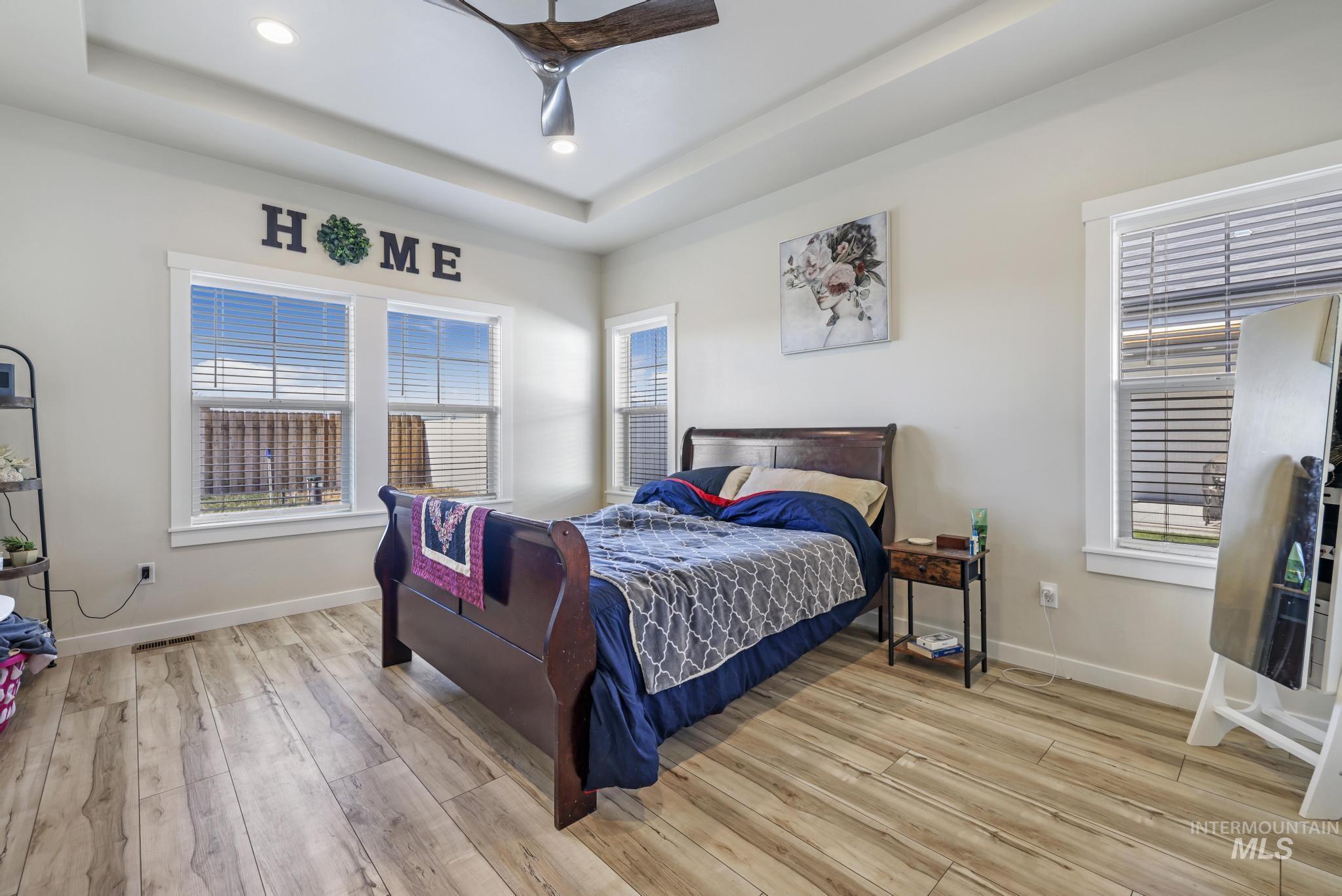 Bedroom with light wood finished floors, a tray ceiling, ceiling fan, and recessed lighting