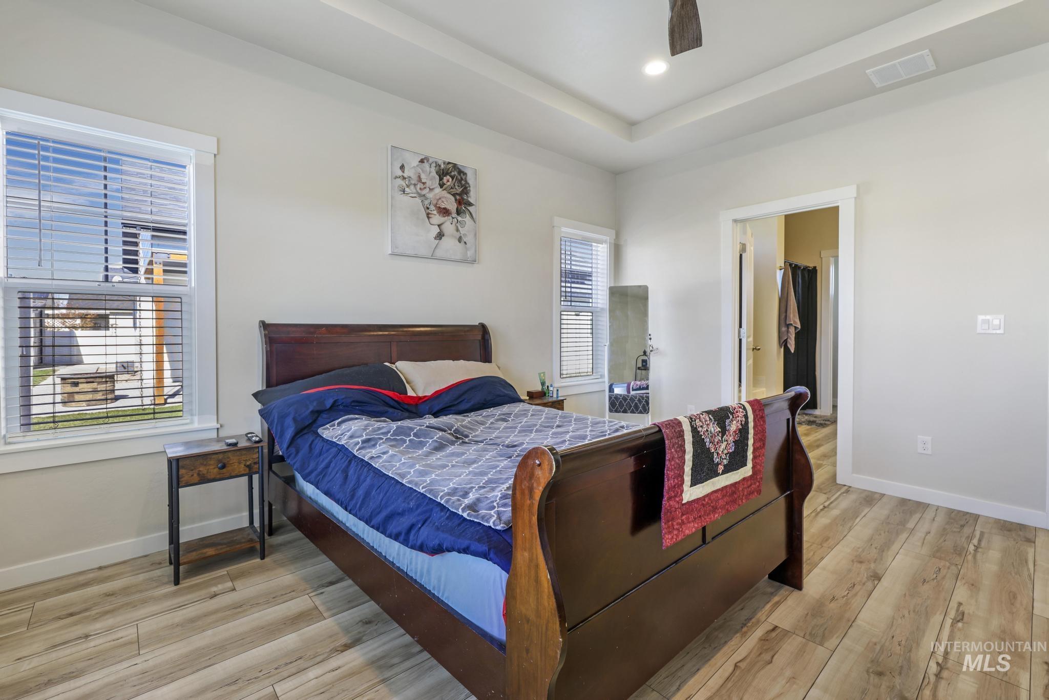 Bedroom with light wood finished floors, a tray ceiling, ceiling fan, and recessed lighting