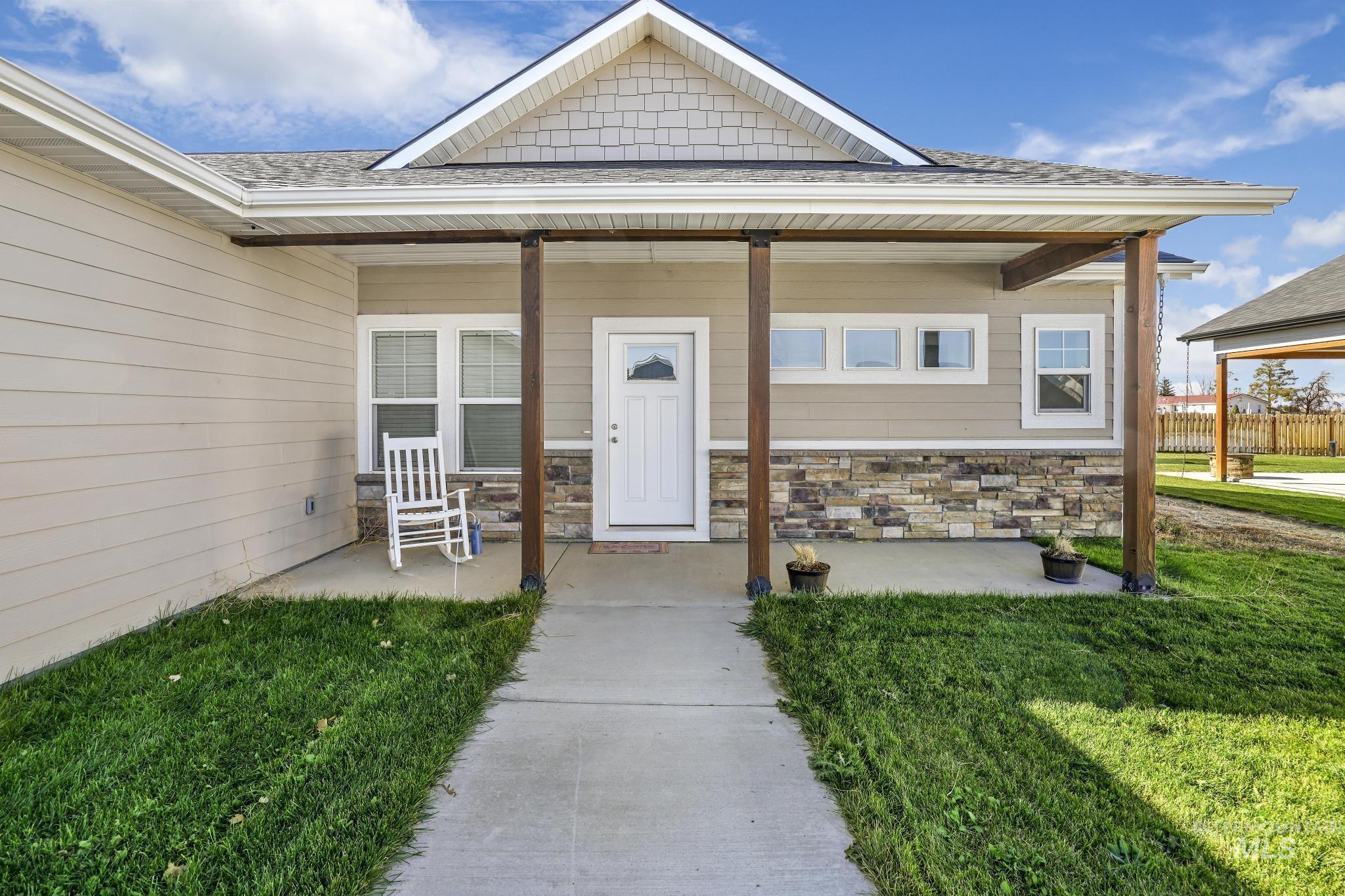 Doorway to property with a shingled roof, stone siding, a porch, and a lawn