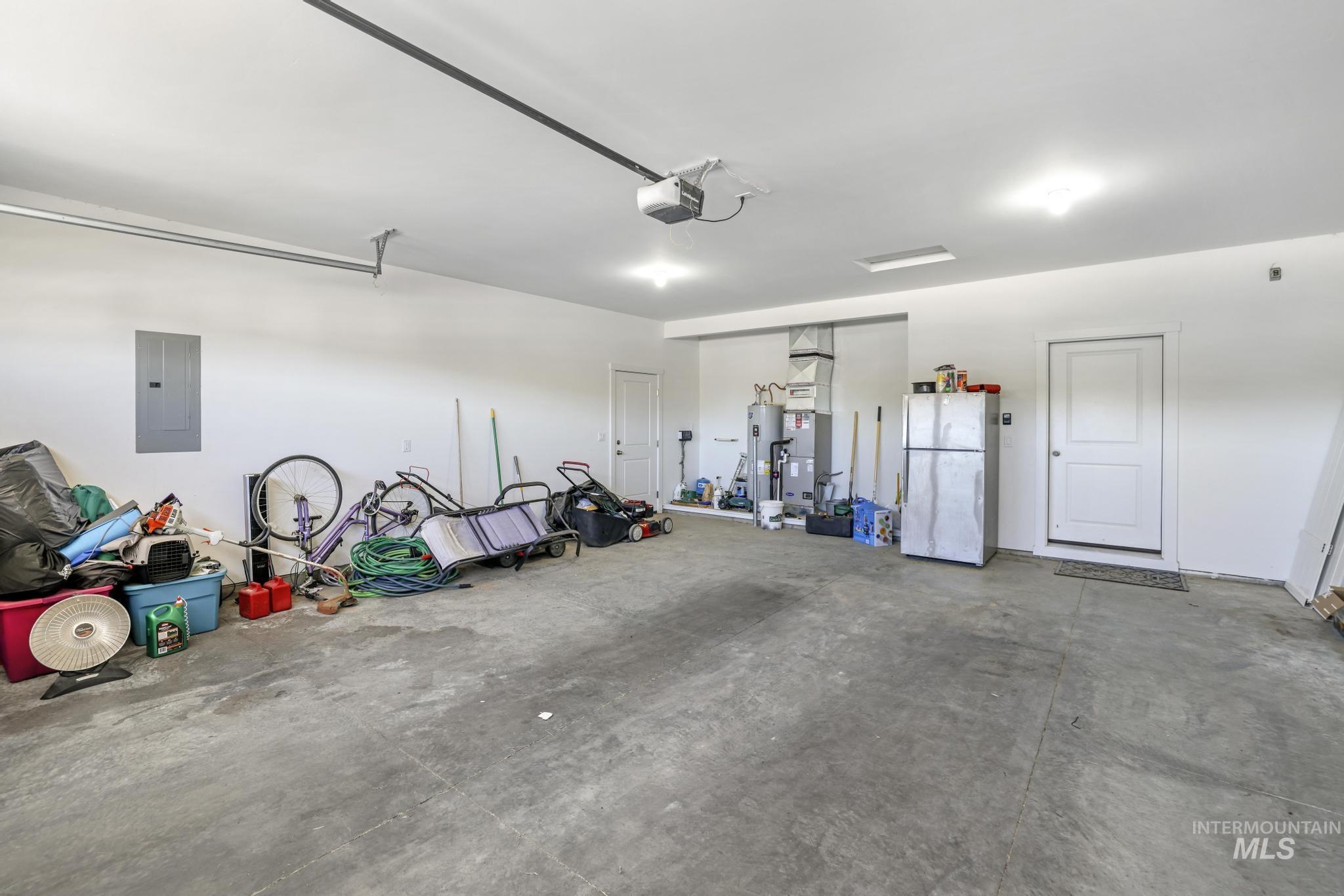 Garage featuring freestanding refrigerator, electric panel, water heater, and a garage door opener