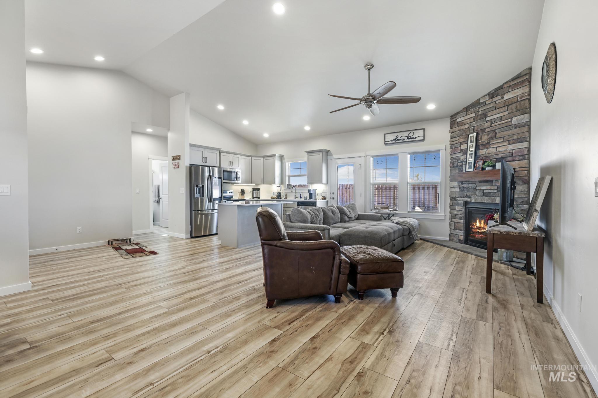 Living room featuring a stone fireplace, light wood-style flooring, ceiling fan, recessed lighting, and high vaulted ceiling
