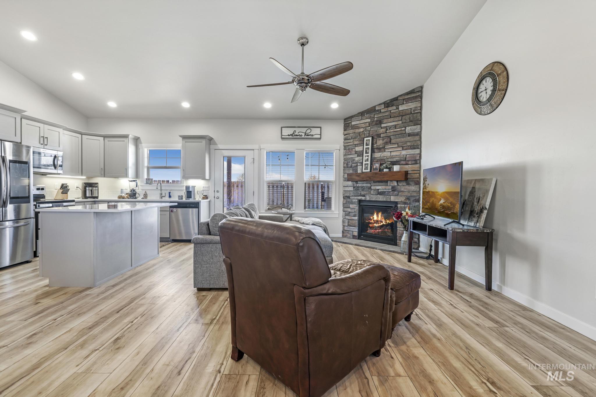 Living room with vaulted ceiling, a fireplace, light wood finished floors, a ceiling fan, and recessed lighting