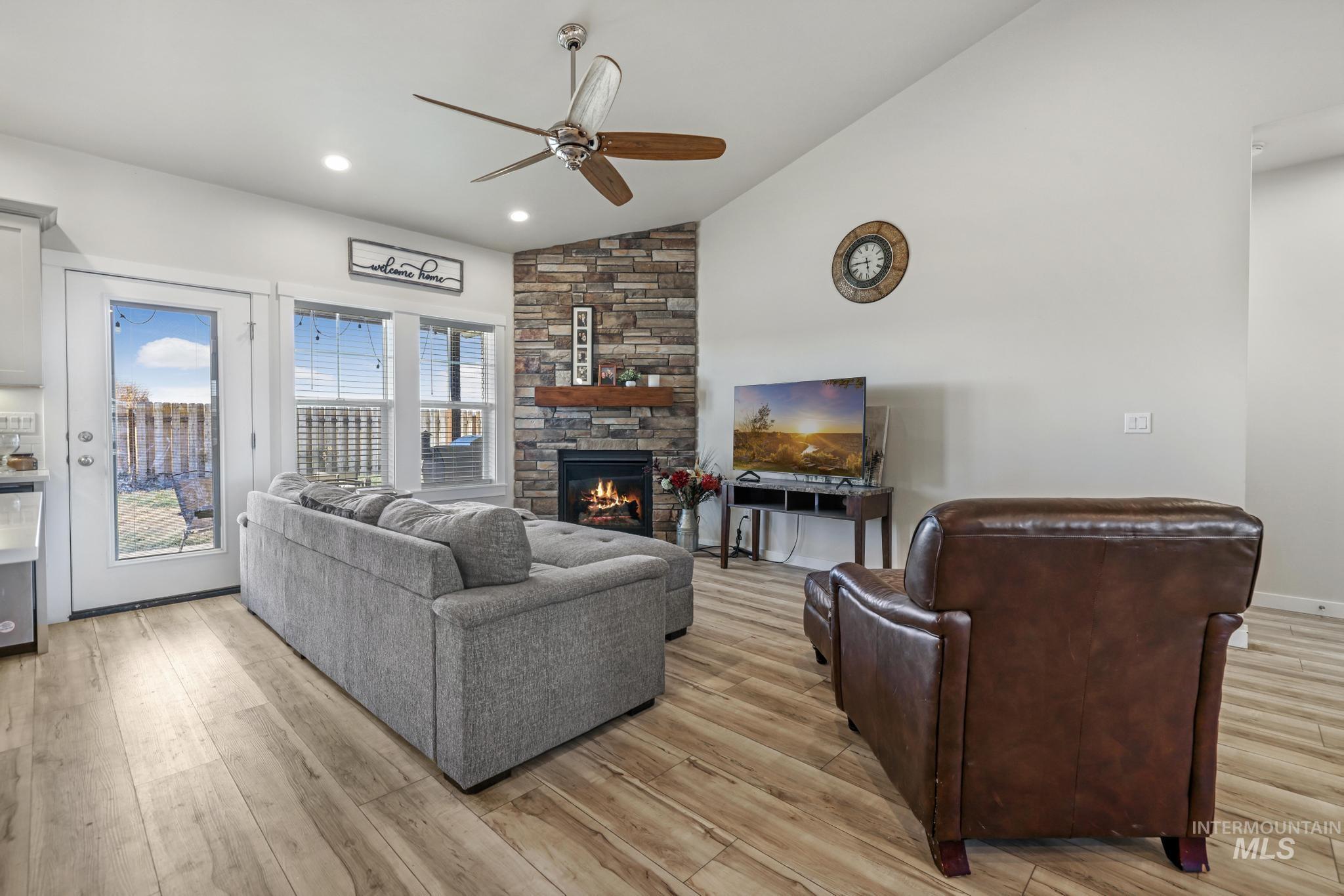 Living area with a ceiling fan, light wood-style floors, a stone fireplace, recessed lighting, and high vaulted ceiling