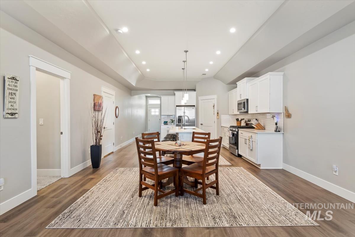 Dining room with dark wood-style flooring, recessed lighting, a raised ceiling, and vaulted ceiling