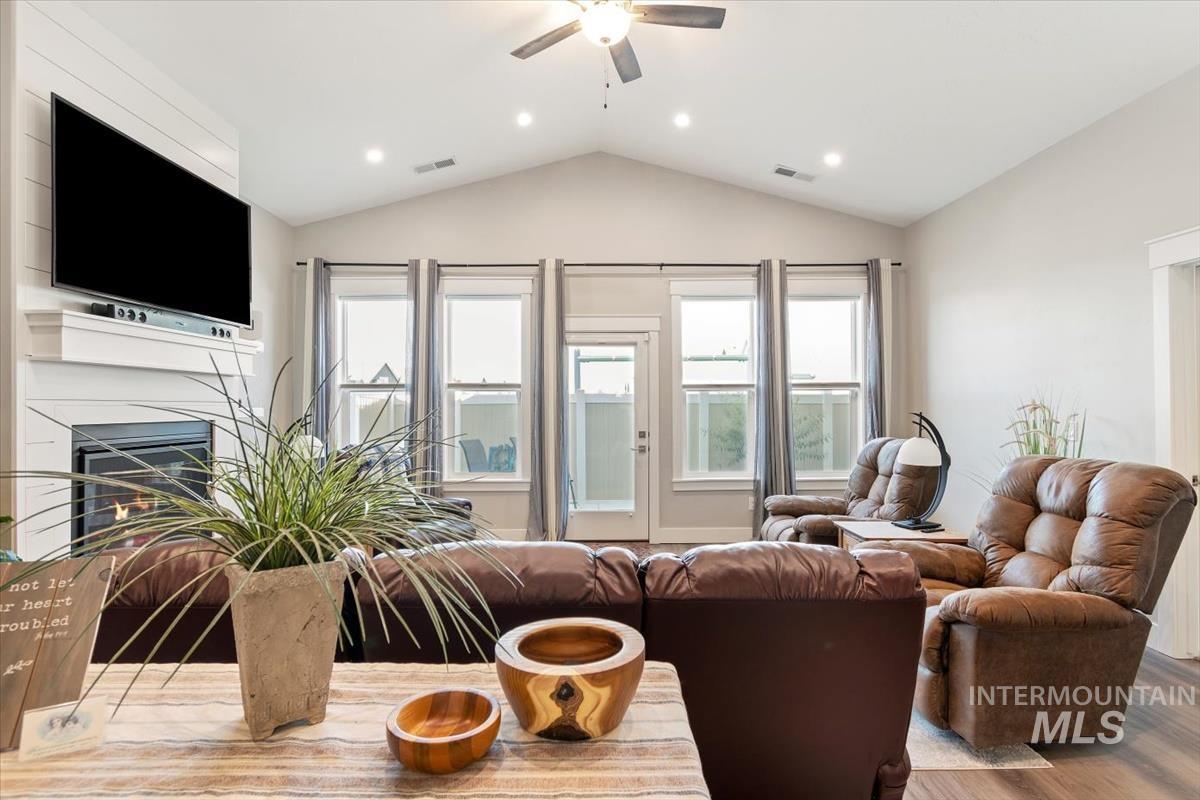Living room with vaulted ceiling, a glass covered fireplace, wood finished floors, ceiling fan, and recessed lighting