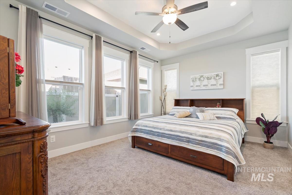 Primary Bedroom featuring a raised ceiling, light carpet, multiple windows, a ceiling fan, and recessed lighting