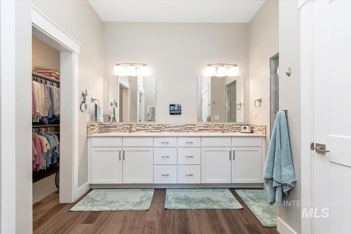 Primary Bathroom featuring double vanity, dark wood-style floors, a walk in closet, and tasteful backsplash