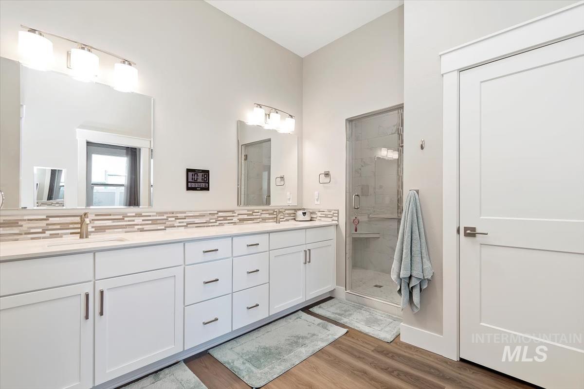 Primary bathroom with a stall shower, double vanity, and light wood-type flooring
